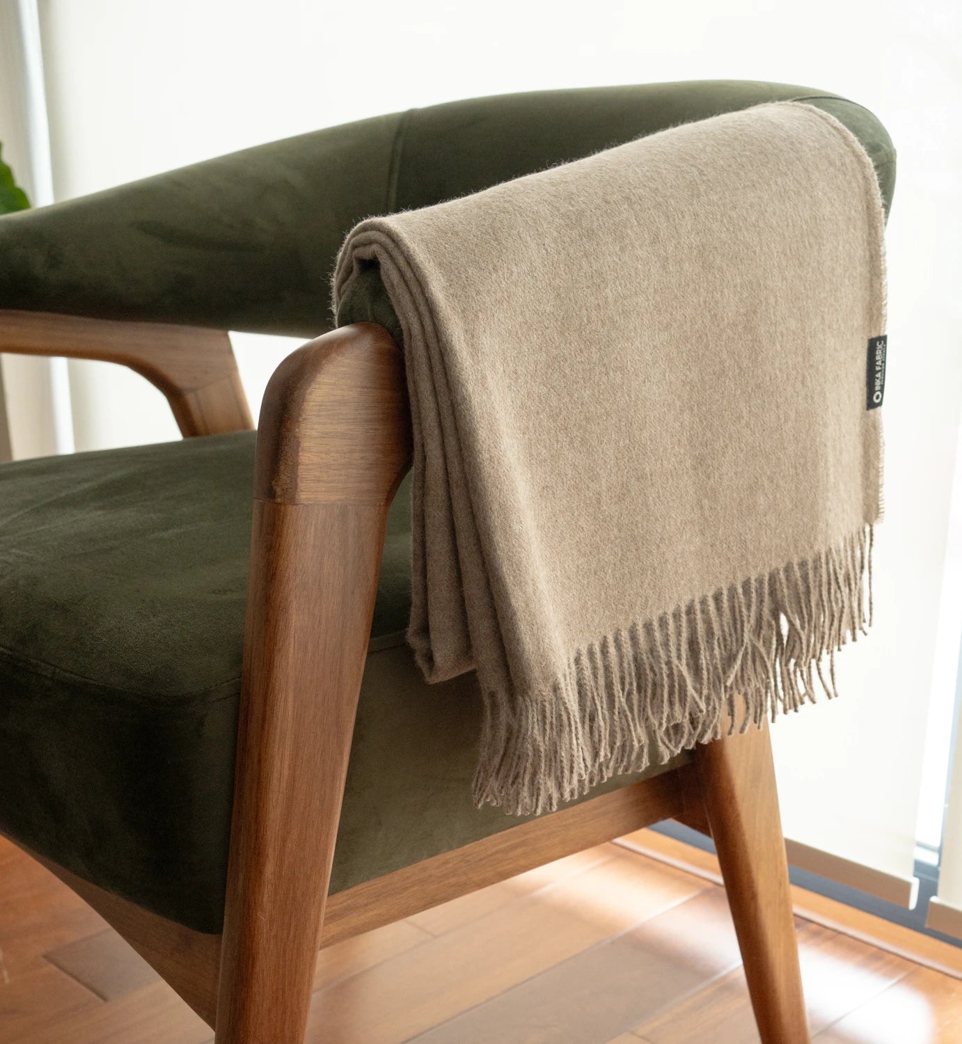 Beige throw blanket draped over a green armchair with wooden legs.