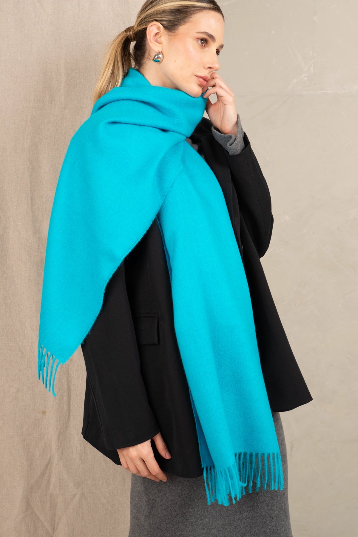 Woman wearing a turquoise scarf and black coat against a beige background