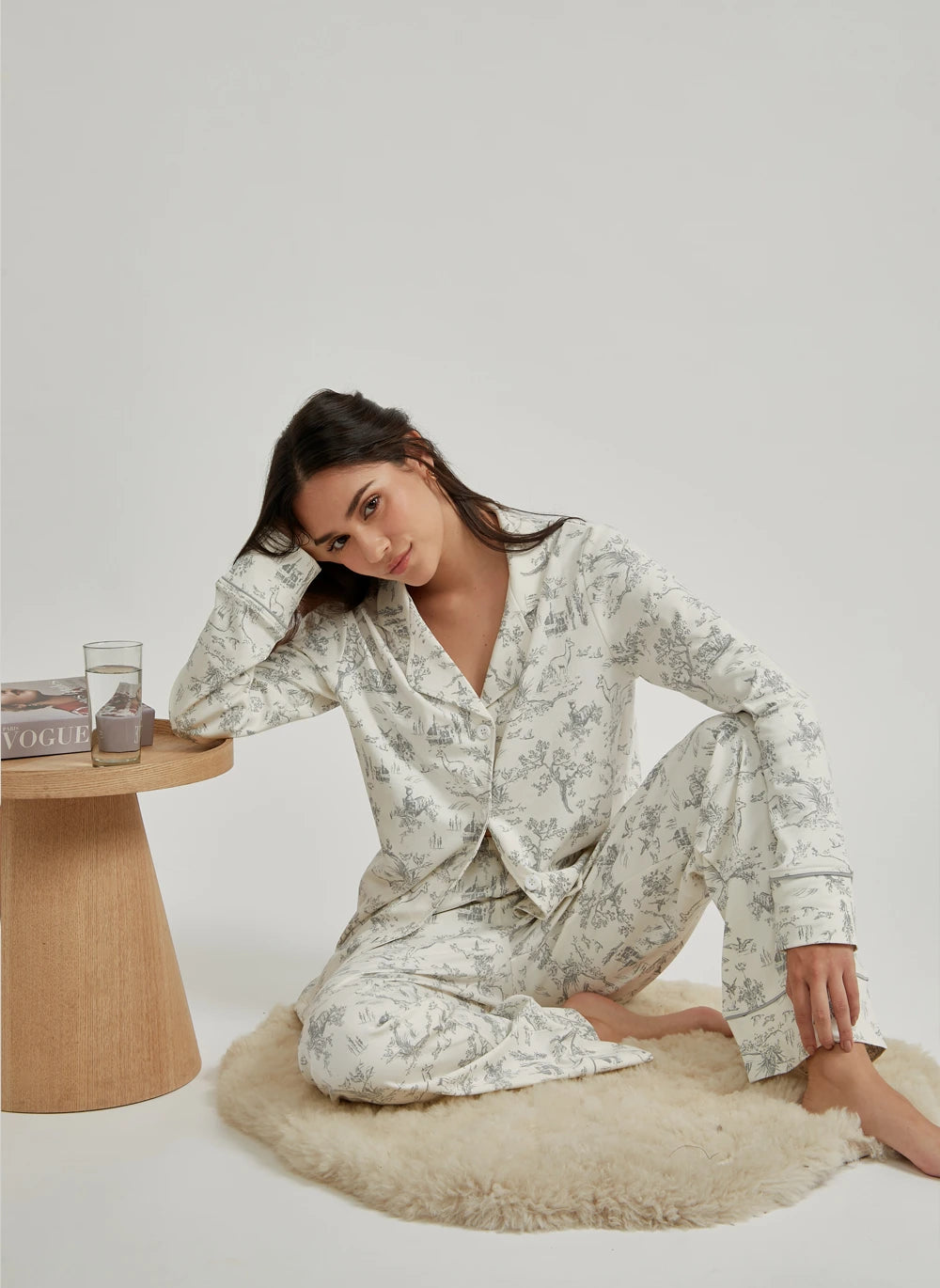 Woman in floral pajama set sitting on a rug with a table and magazine in the background