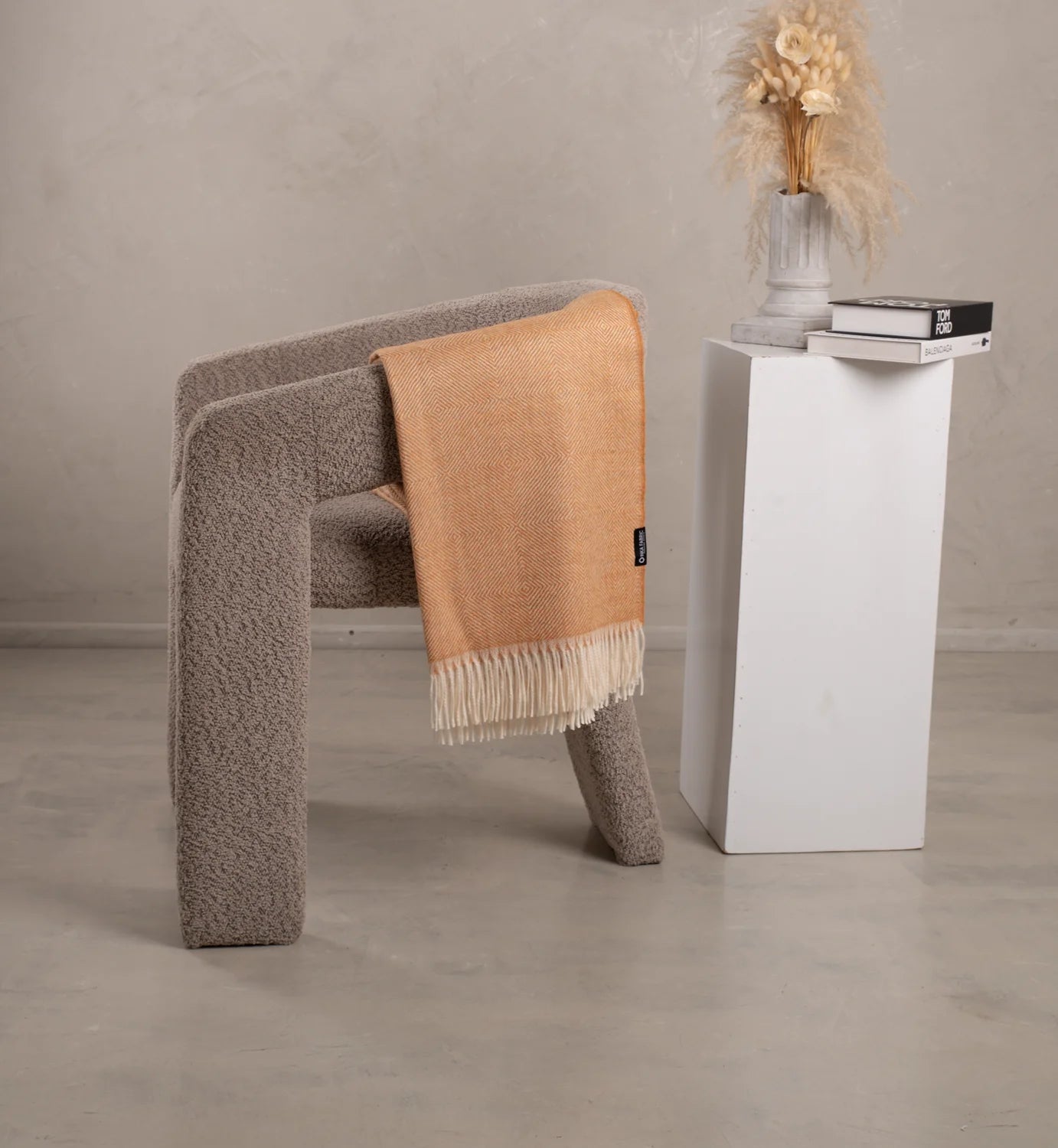 A chair with an alpaca amber blanket draped over it next to a white pedestal table.