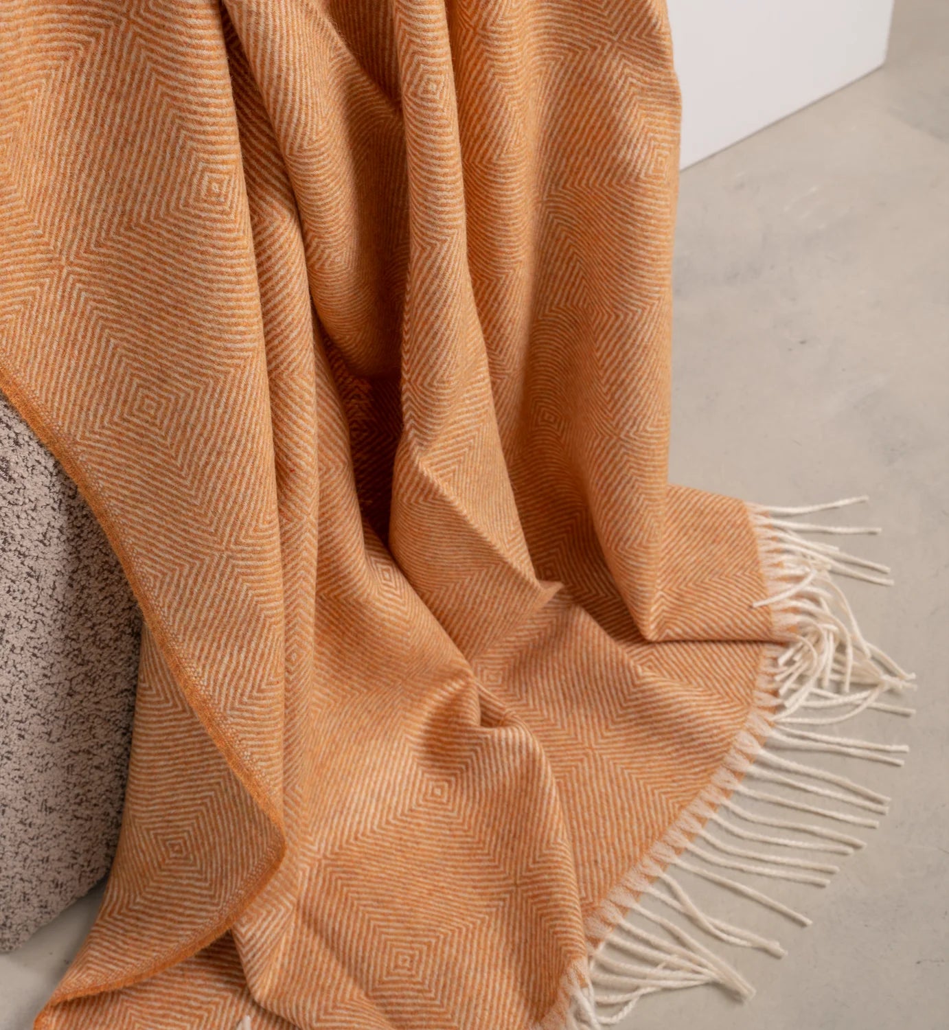 Orange woven blanket with white fringe on a neutral background