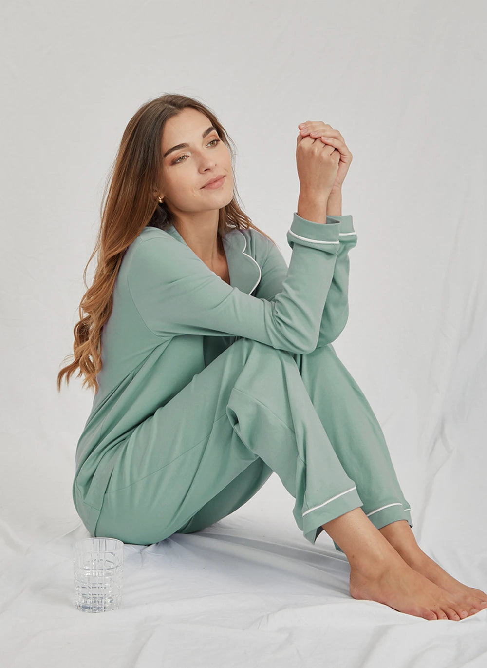 Woman wearing a green pajama set sitting on a white bed.