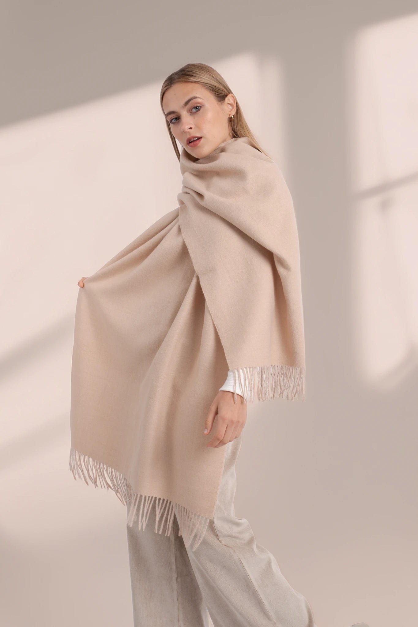Woman wearing a beige scarf with fringe details against a neutral background