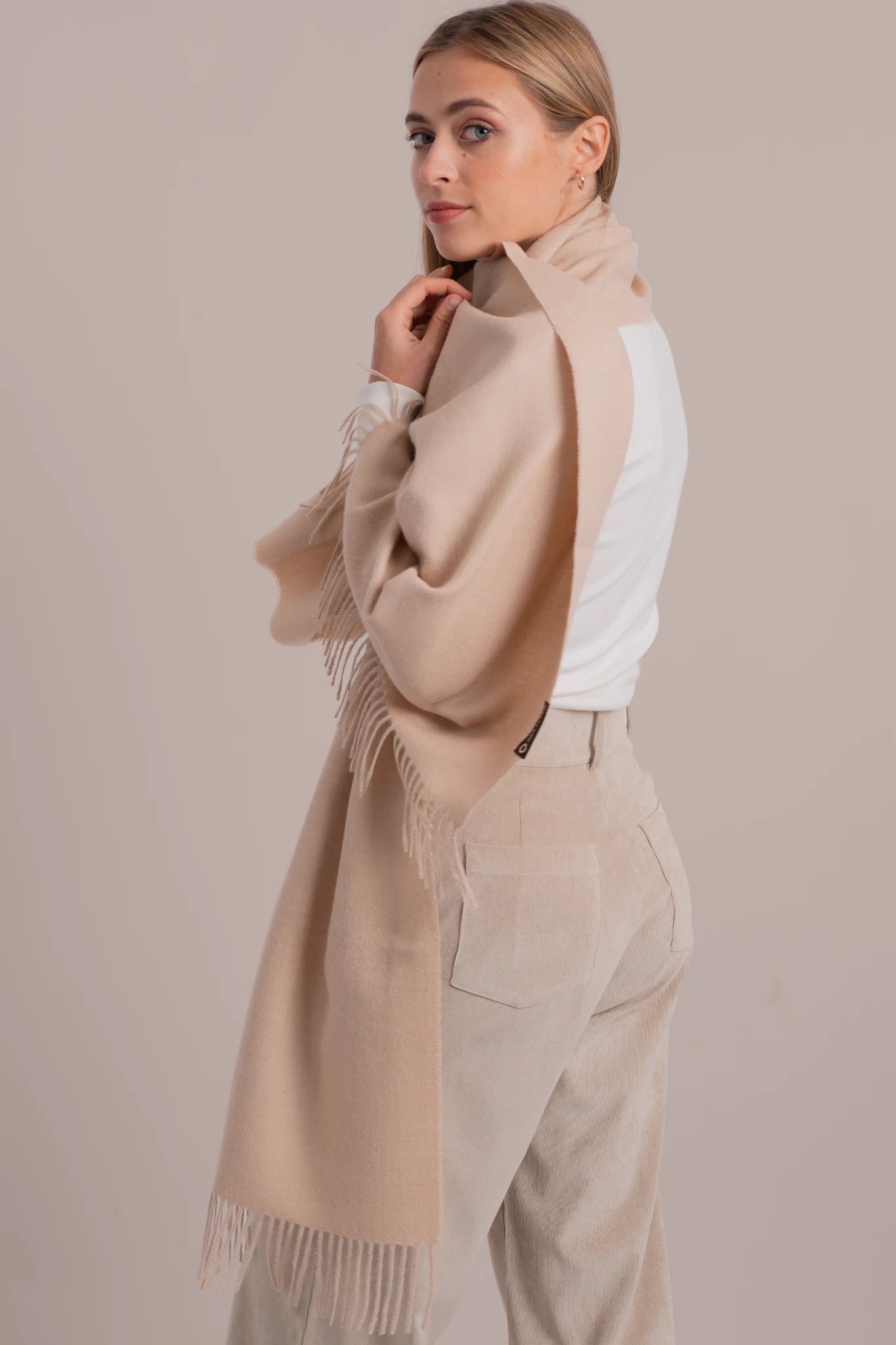 Woman wearing a beige scarf and white top against a beige background