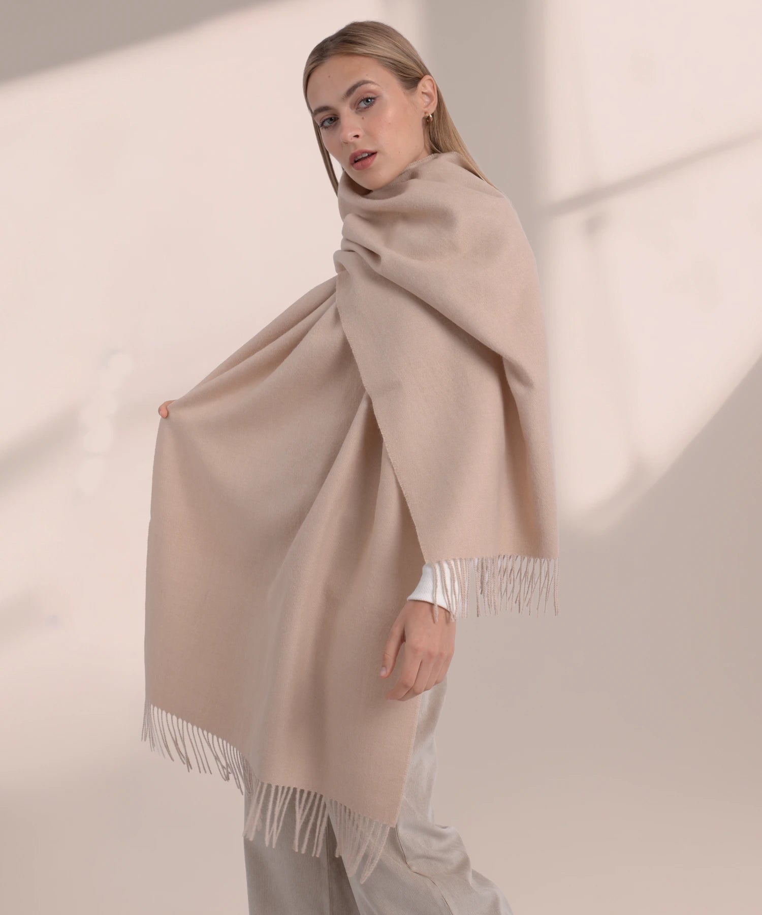 Woman wearing a beige scarf with fringe details on a plain background