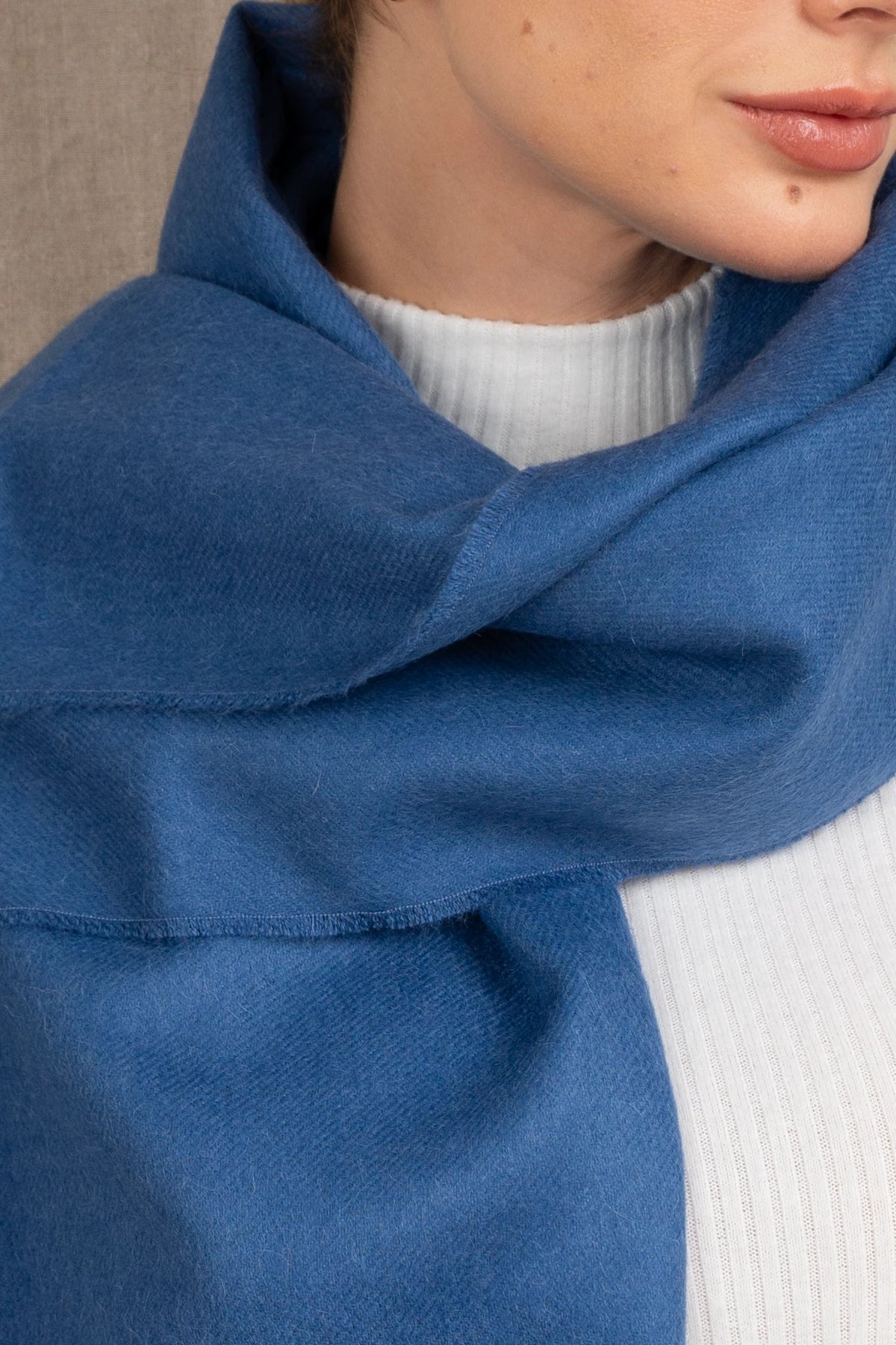 Close-up of a person wearing a blue 100% baby alpaca scarf and white sweater.