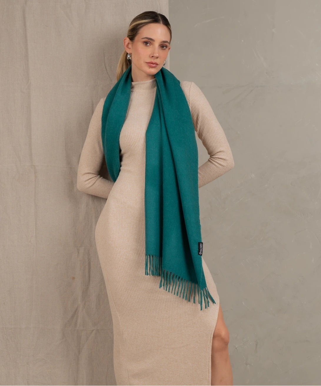 Woman wearing a beige dress and teal scarf against a plain background