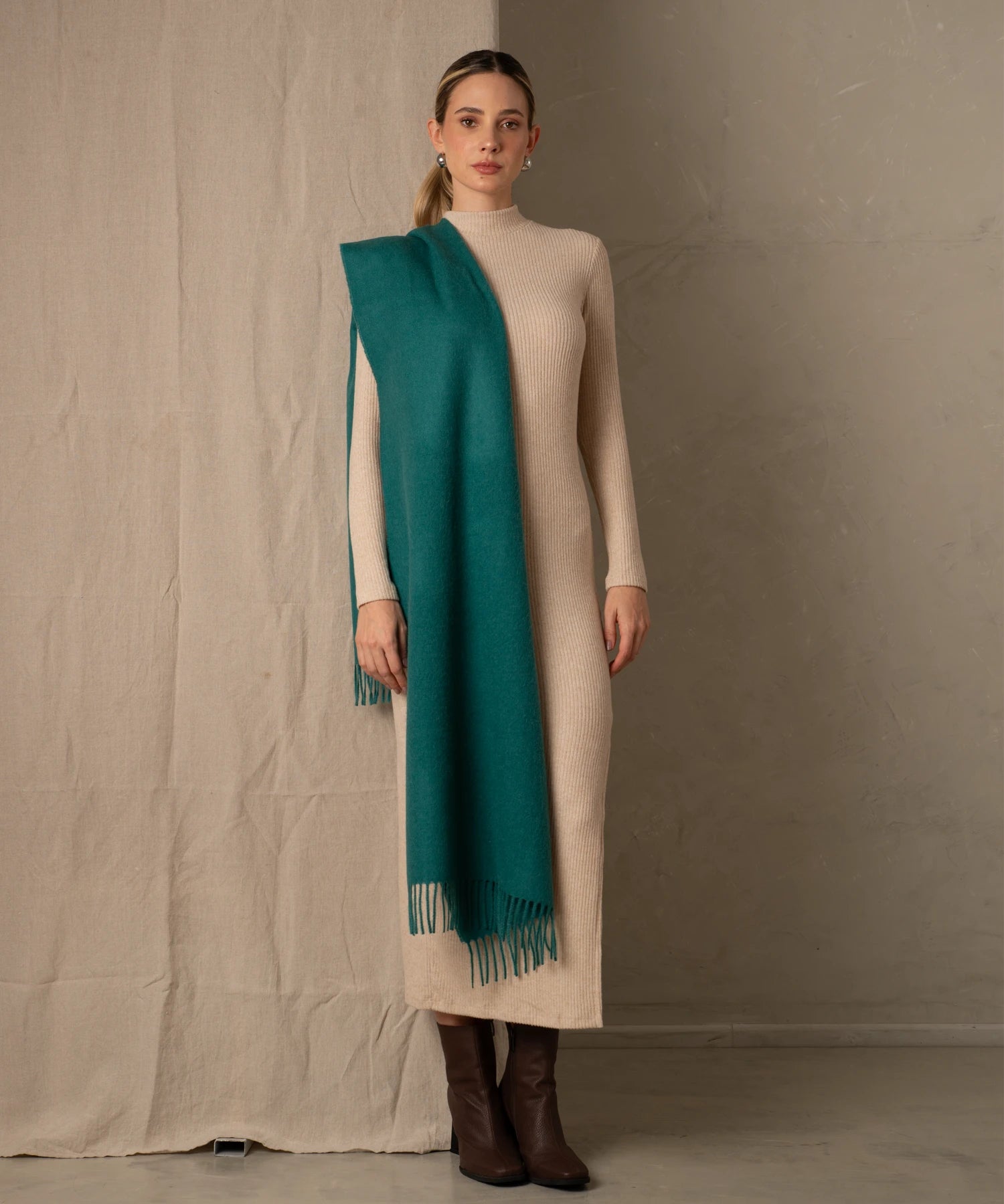 Woman wearing a long beige dress with a teal scarf against a neutral background