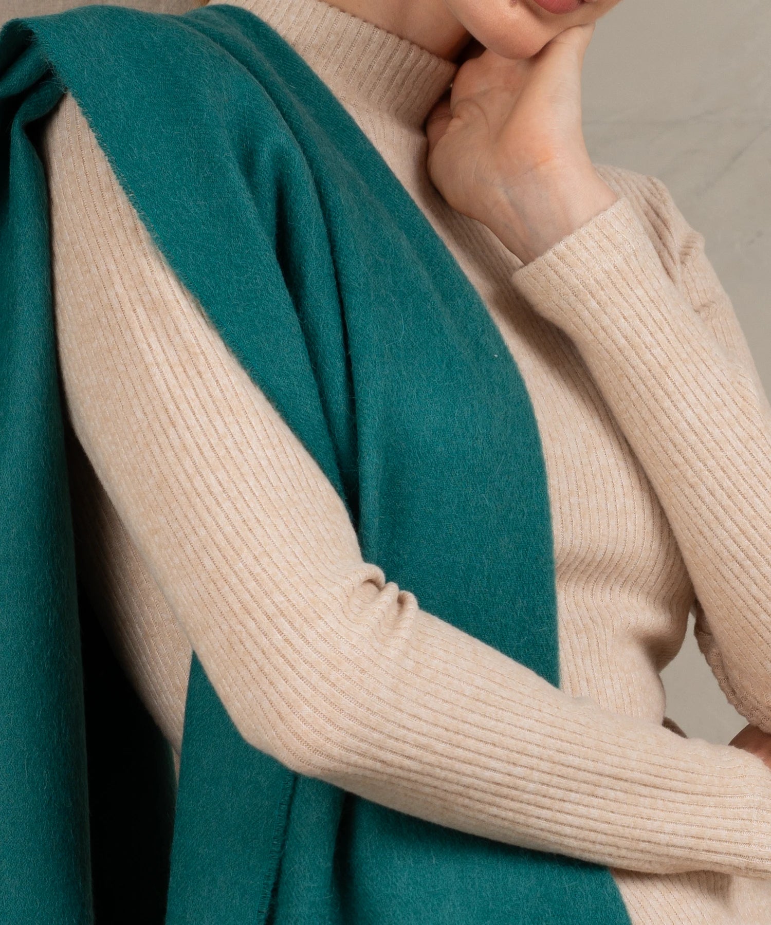 Close-up of a person wearing a teal coat over a beige sweater.