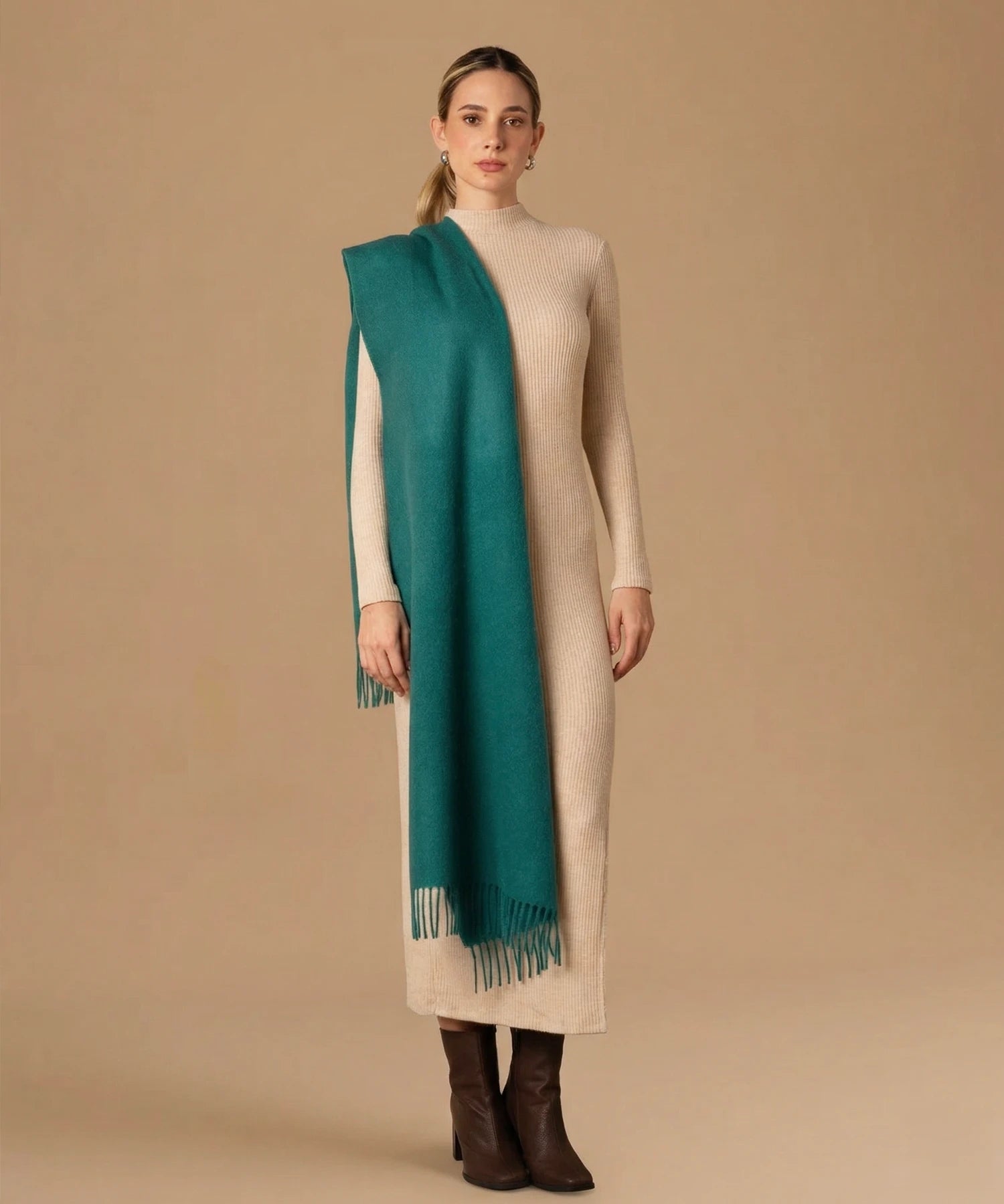 Woman wearing a long teal scarf and beige dress against a beige background