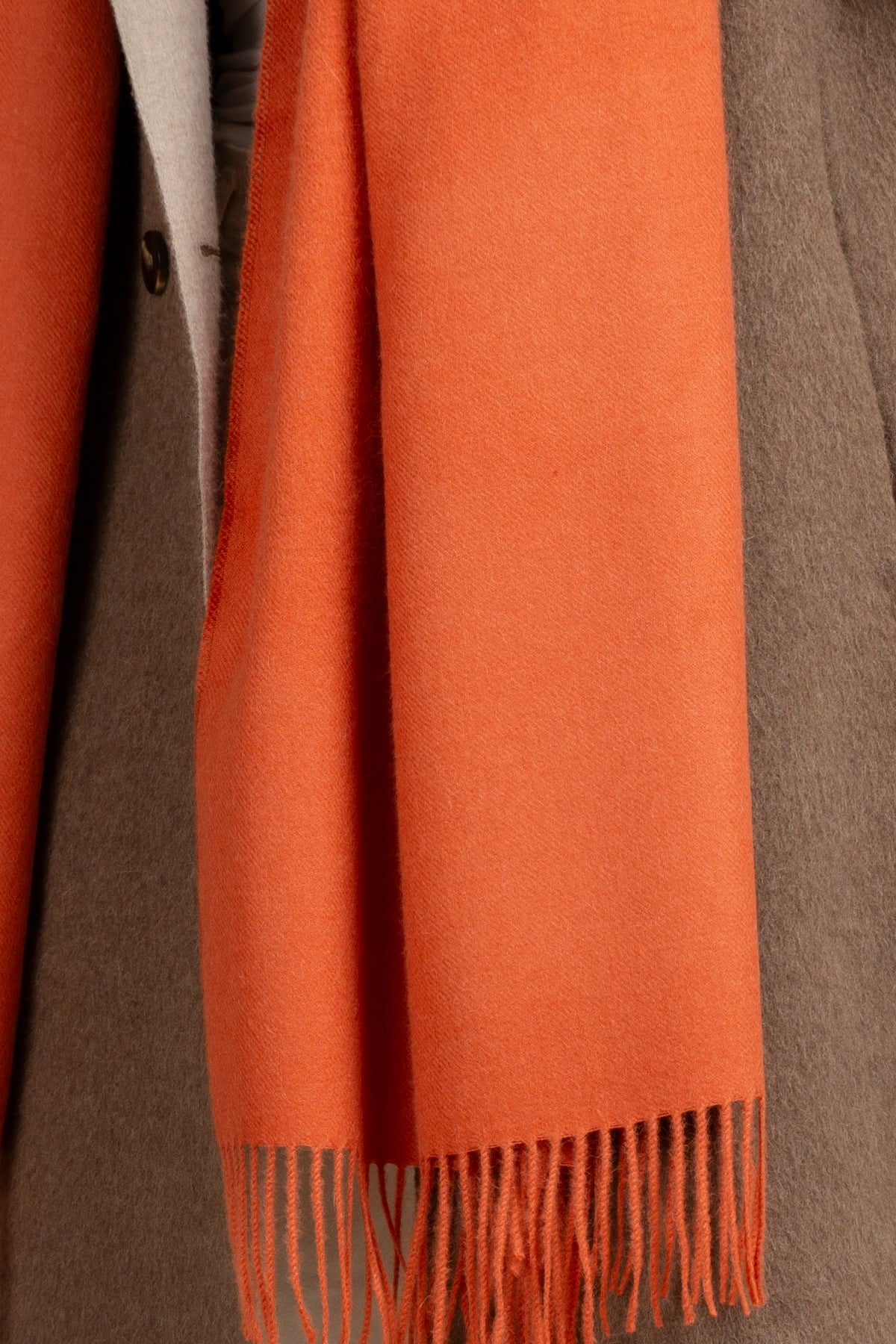 Close-up of an orange scarf with fringes draped over a brown garment.