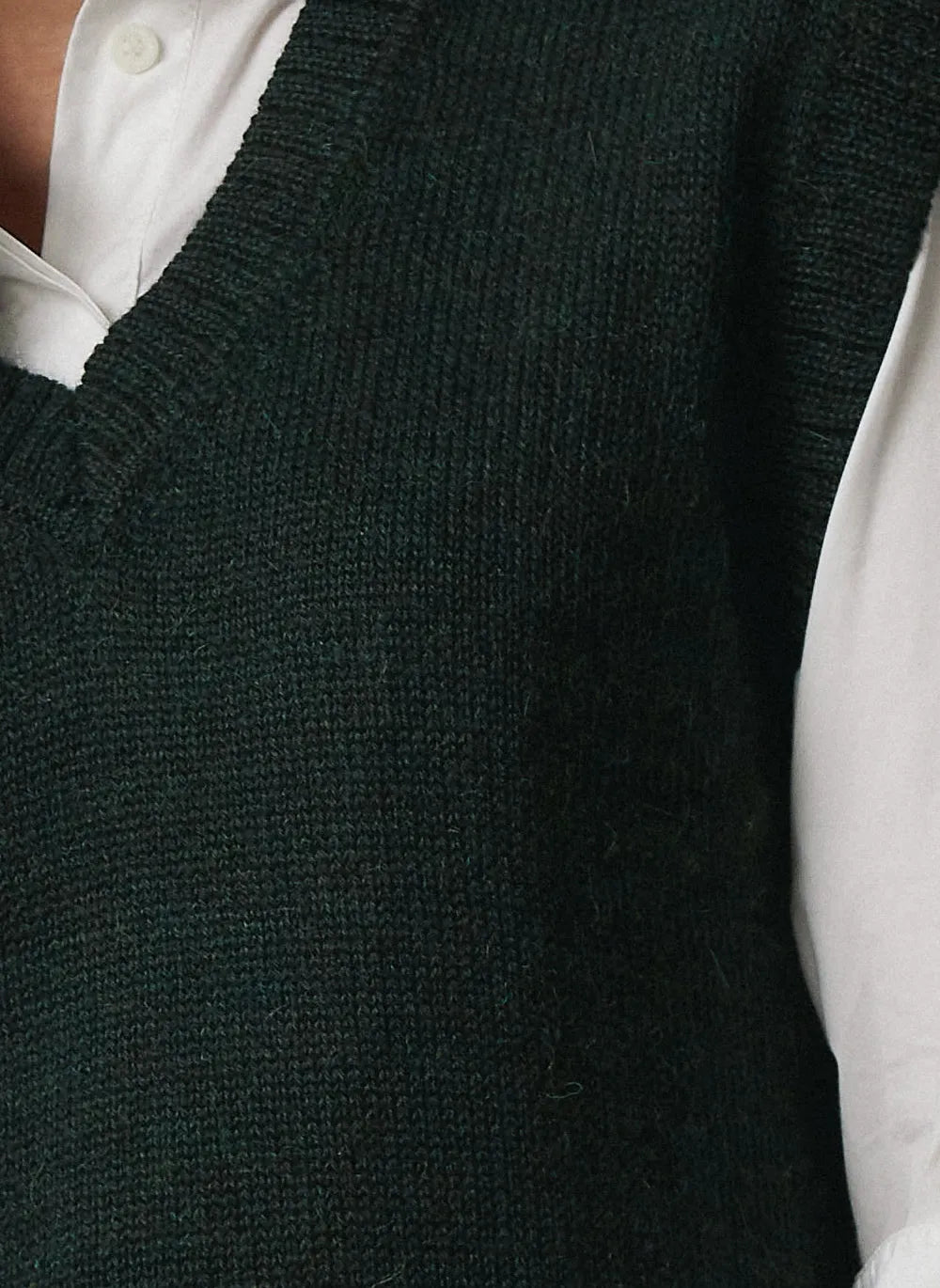 Close-up of a dark forest green ribbed knit sweater vest worn over a white collared shirt.