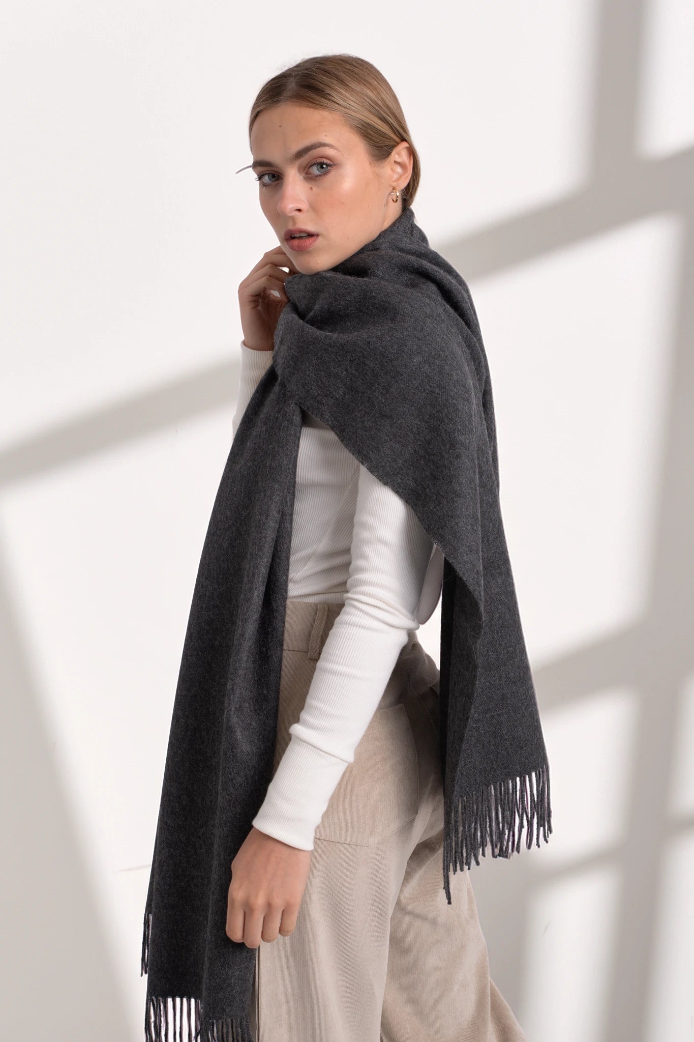 Woman wearing a dark gray scarf with fringes on a white background
