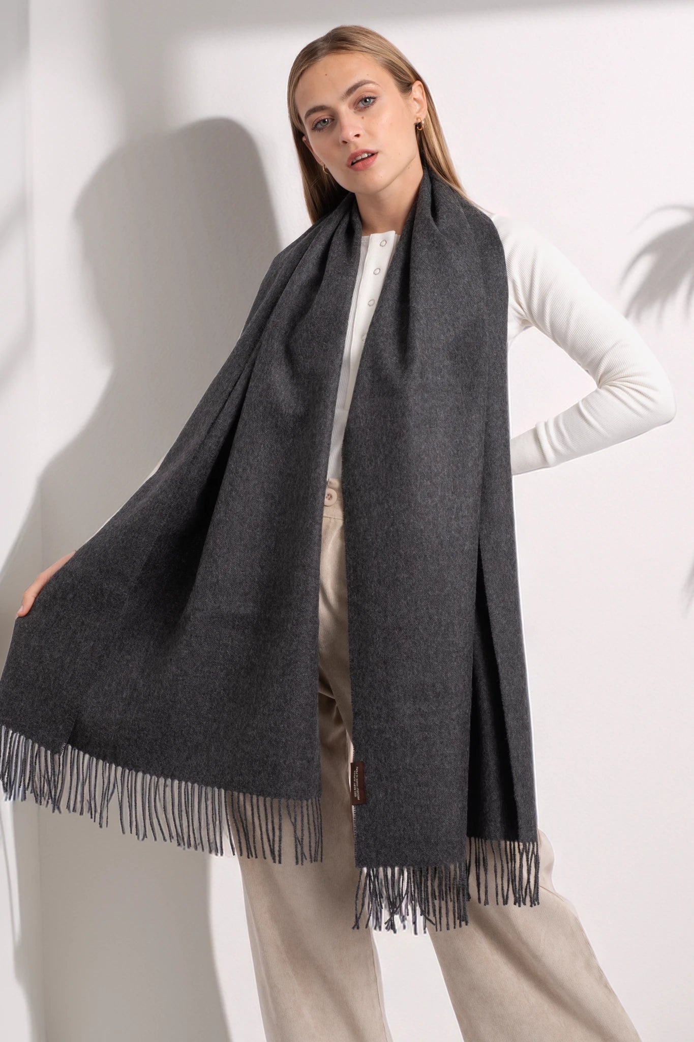 Woman wearing a dark gray scarf with fringes on a white background