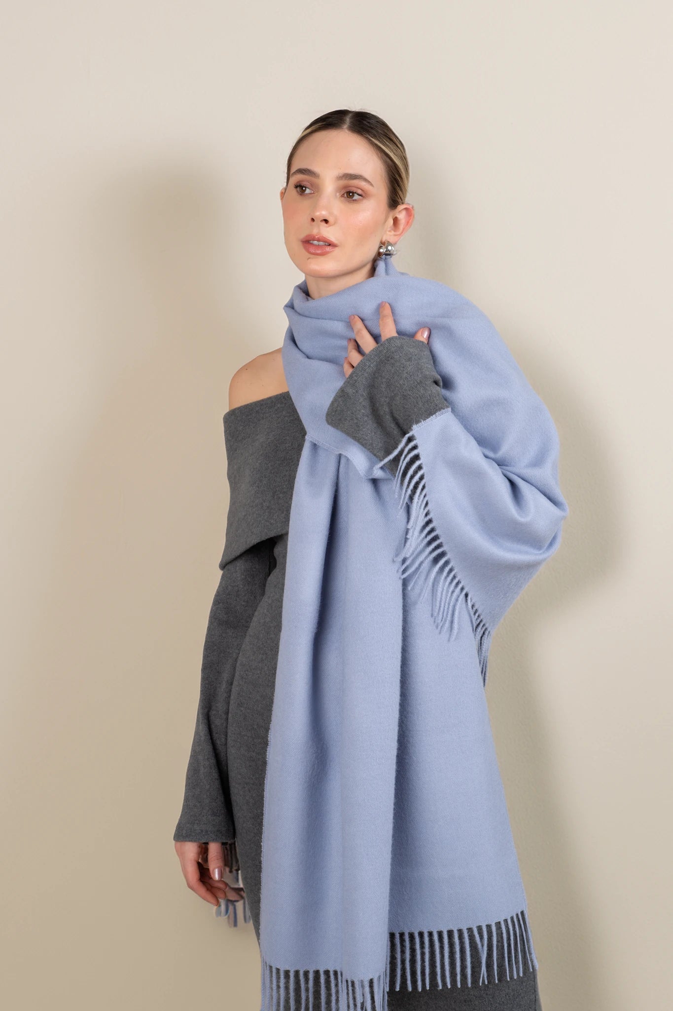 Woman wearing a light blue scarf with fringe details on a beige background