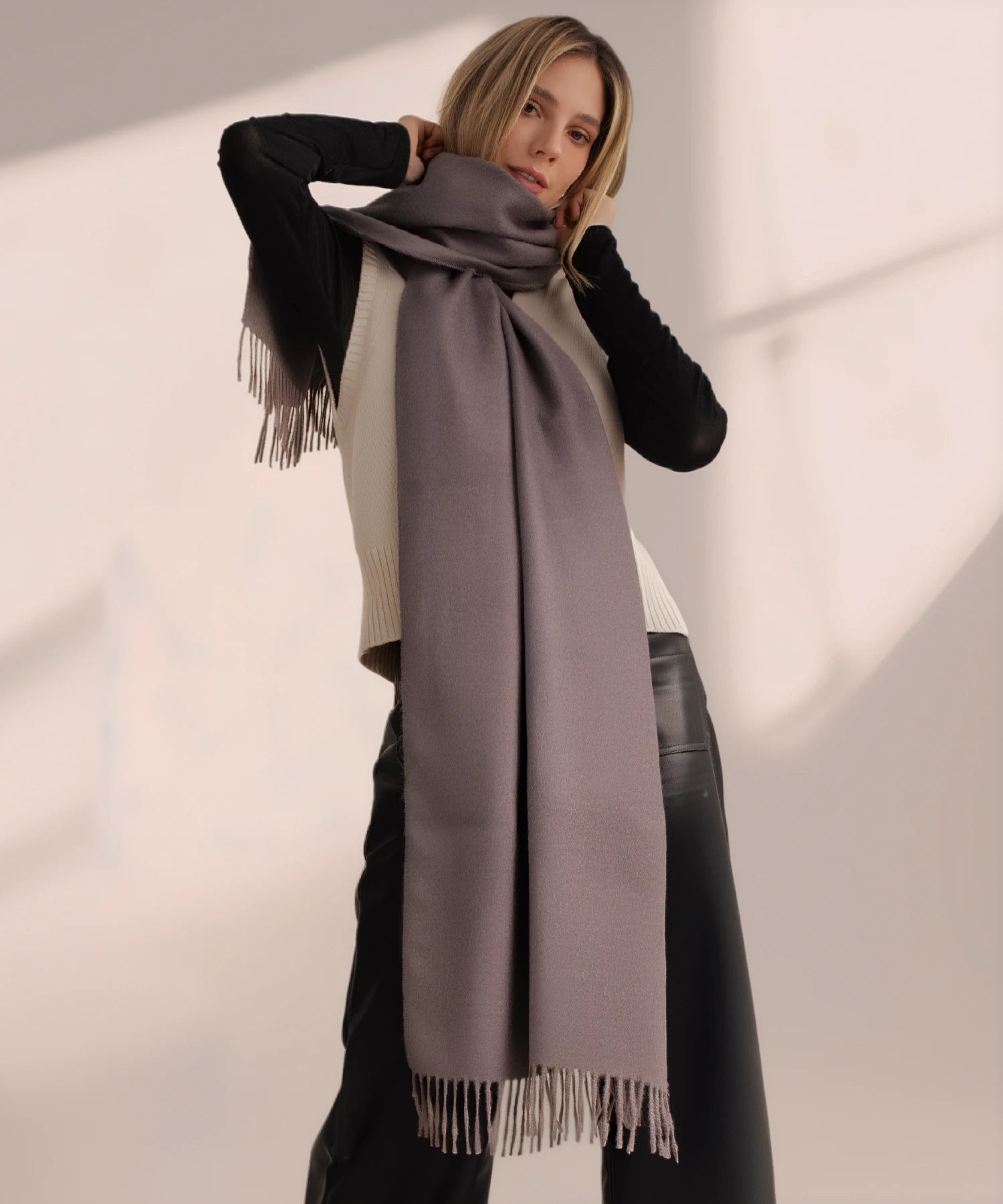 Woman wearing a long gray scarf with black edges on a plain background