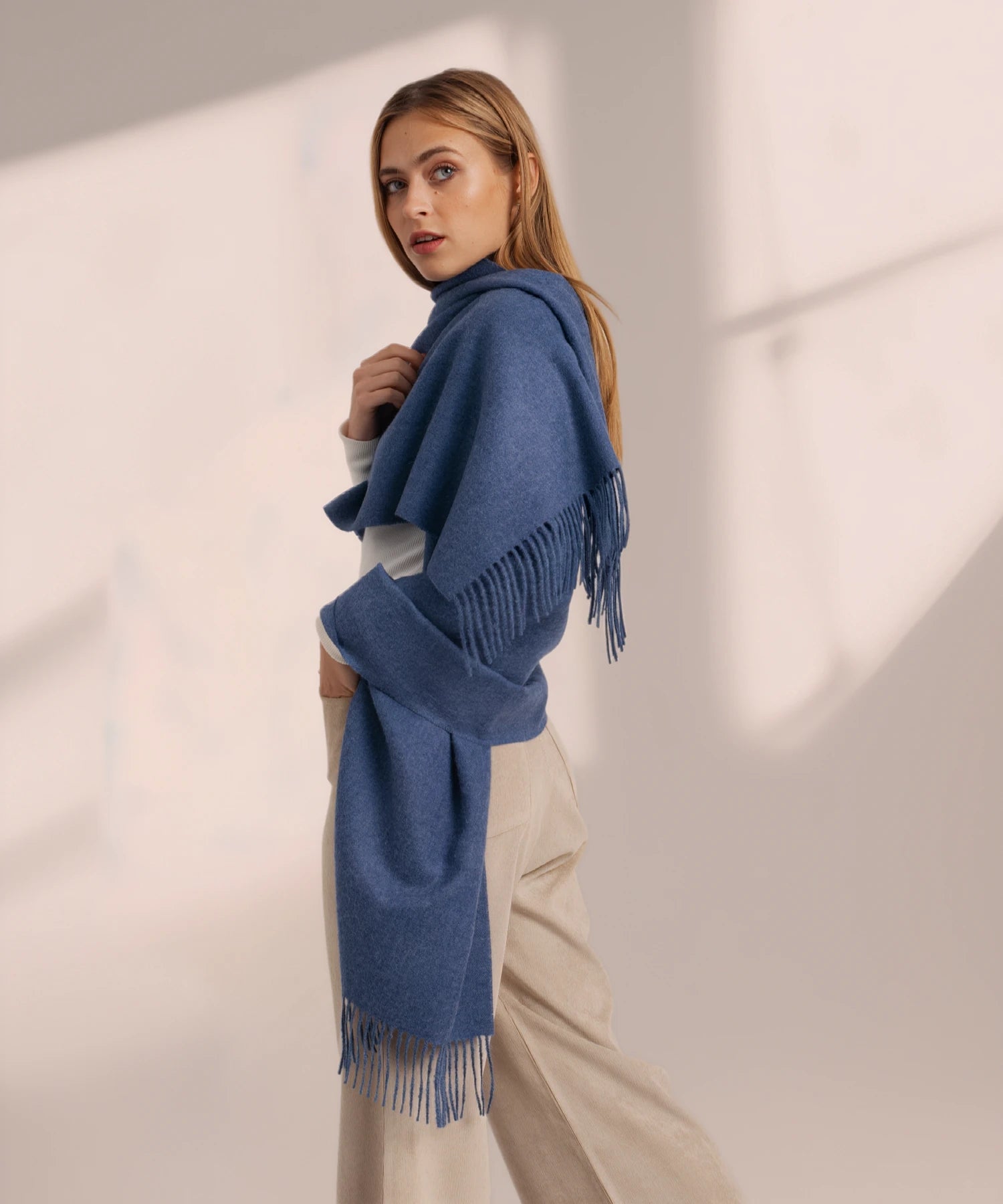 Woman wearing a blue fringed scarf against a neutral background