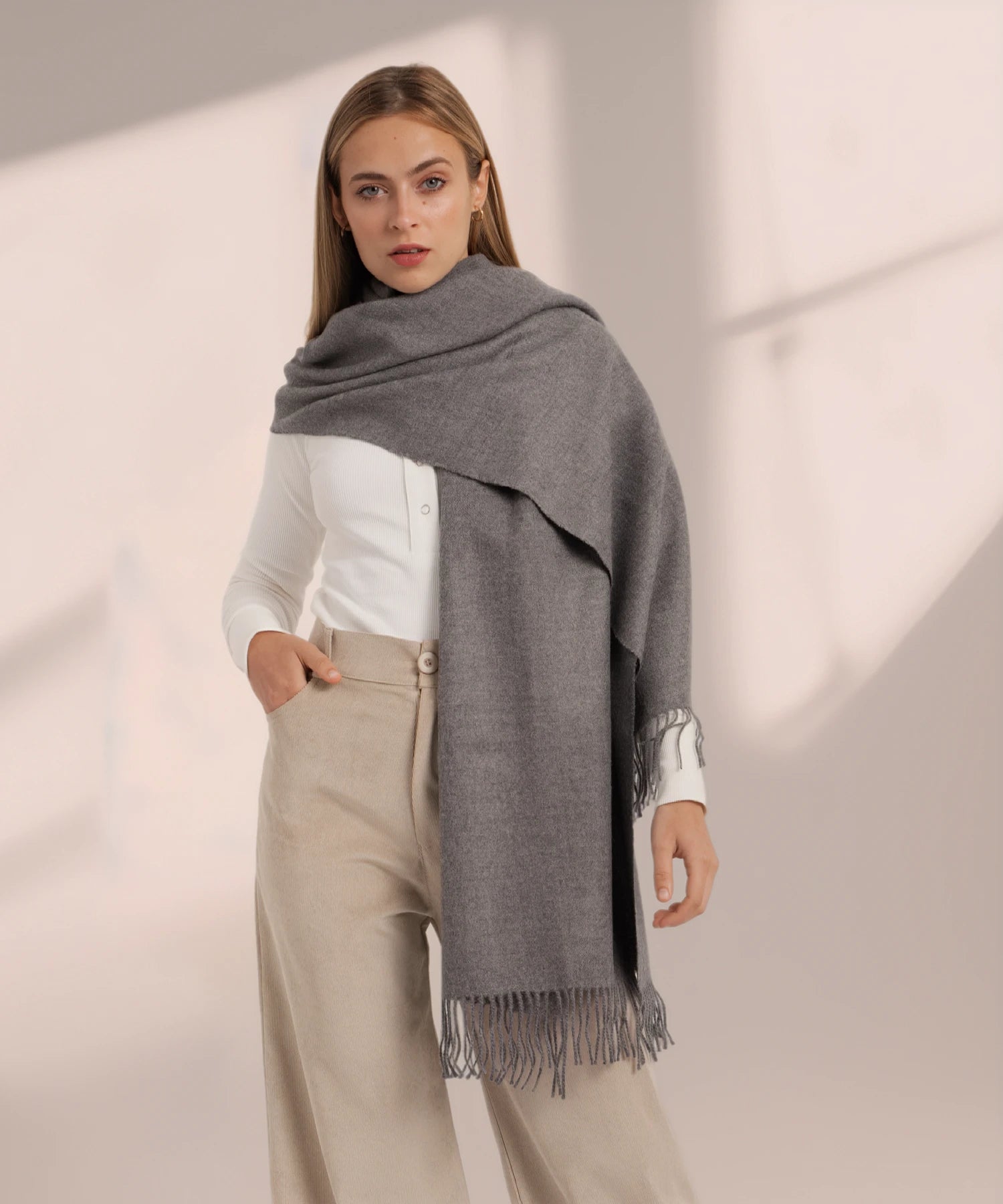 Woman wearing a gray scarf with fringe on a beige background