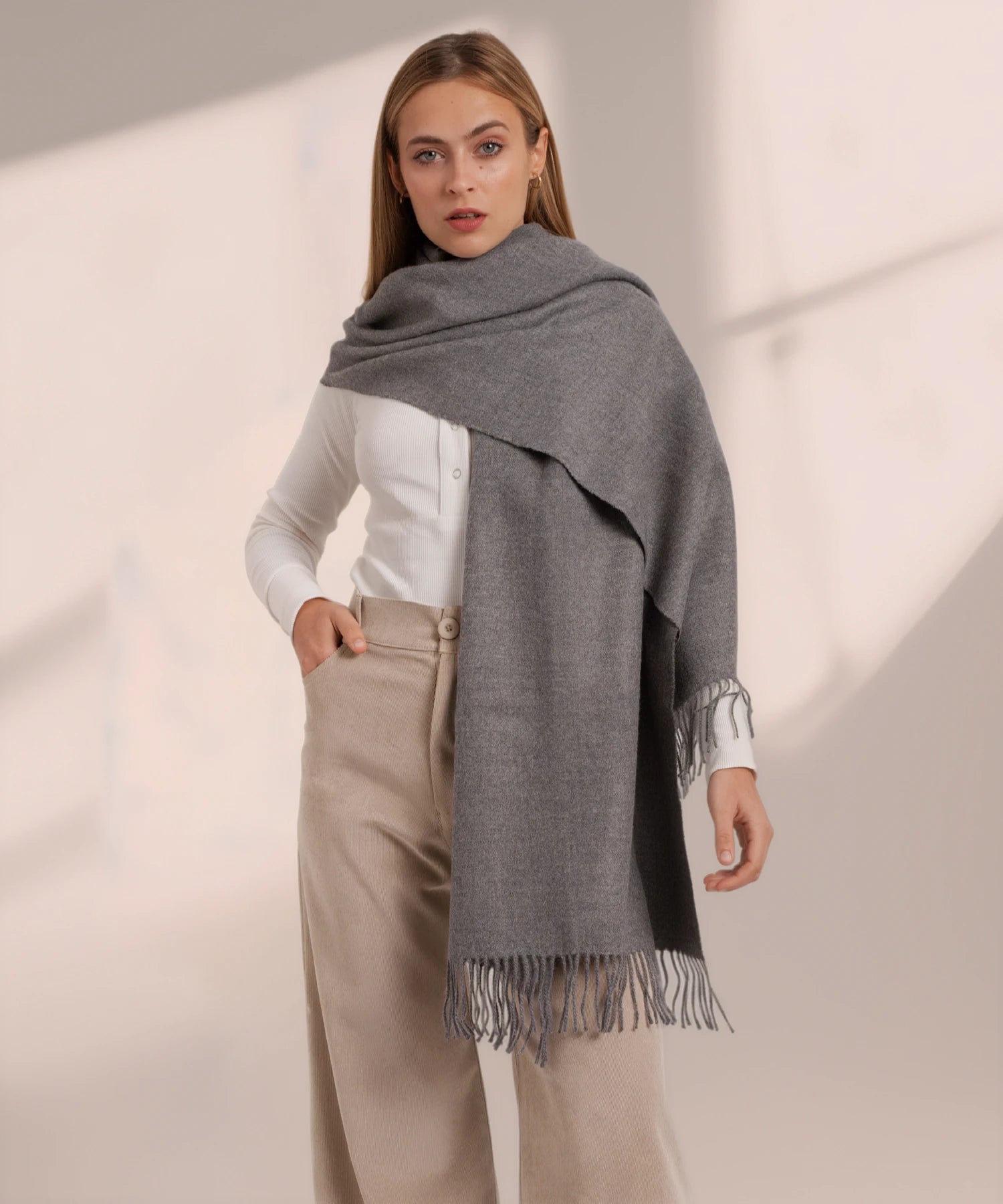 Woman wearing a gray scarf with fringe on a plain background