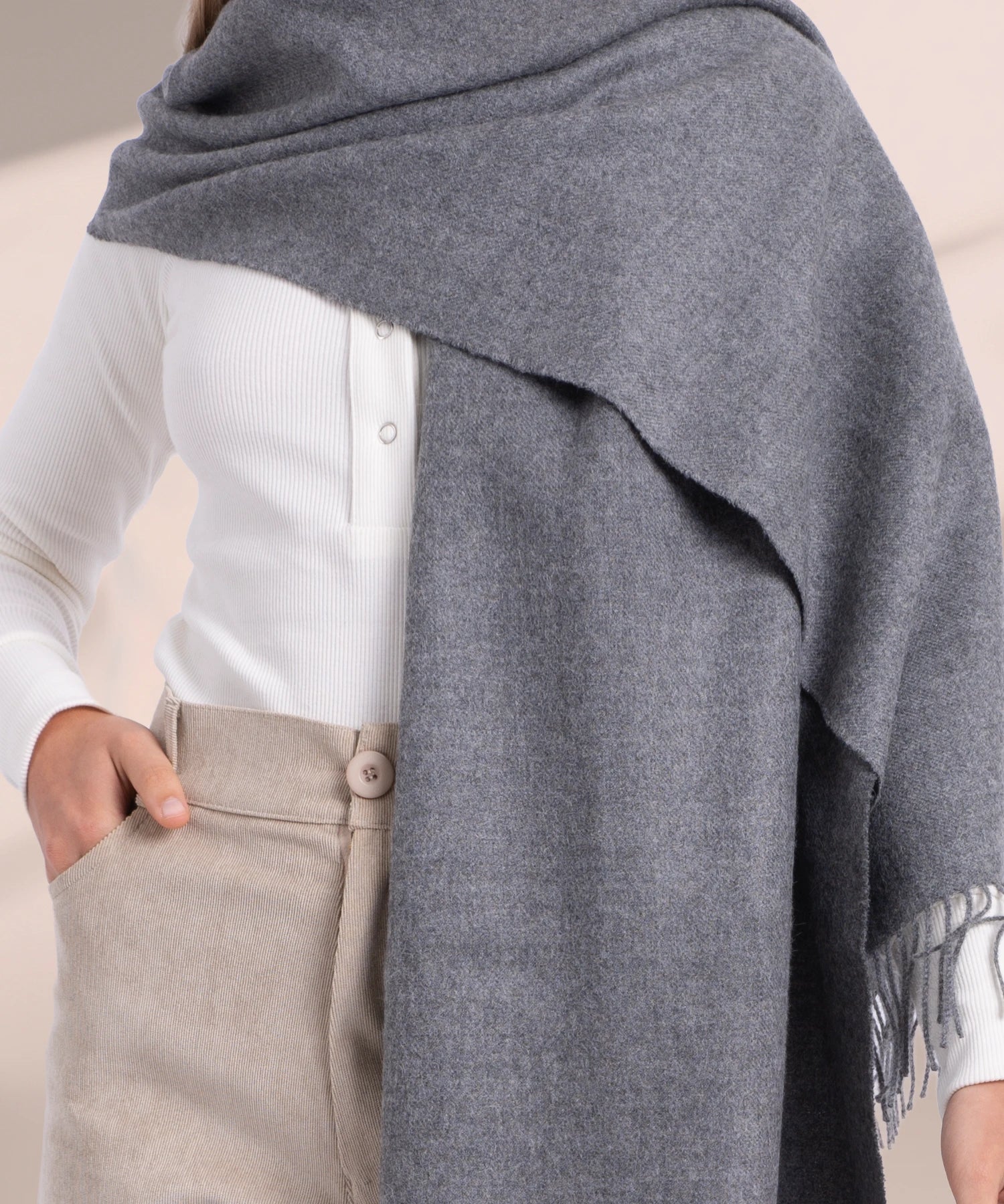 Person wearing a gray shawl over a white shirt and beige pants on a neutral background