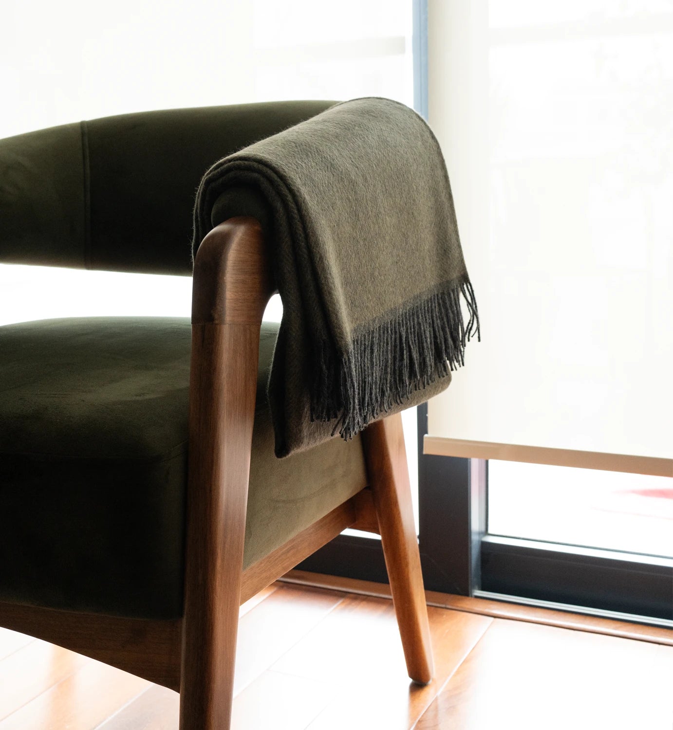 Green blanket draped over a wooden chair in a bright room with large windows.