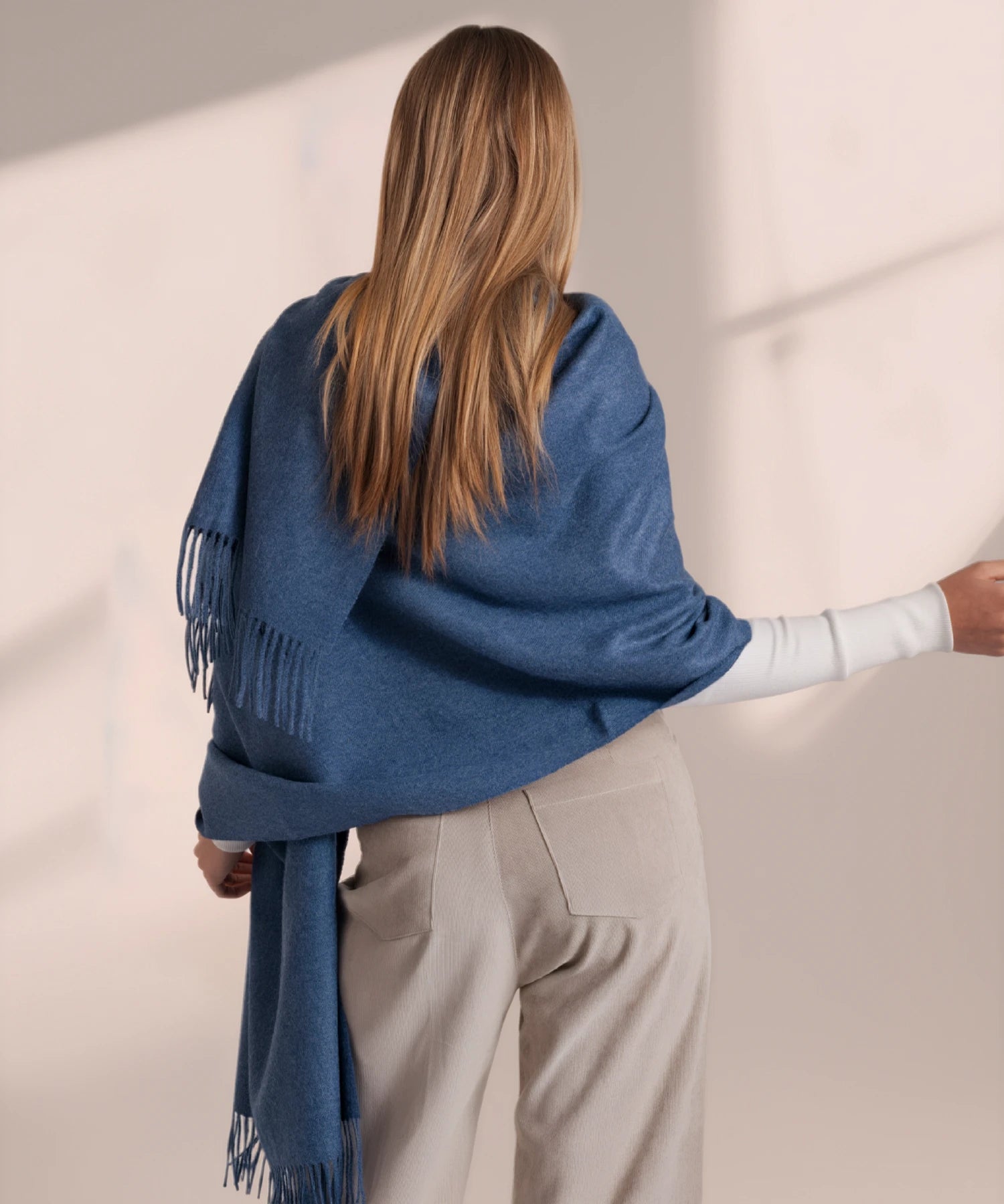 Person wearing a blue scarf with fringe, standing against a plain background