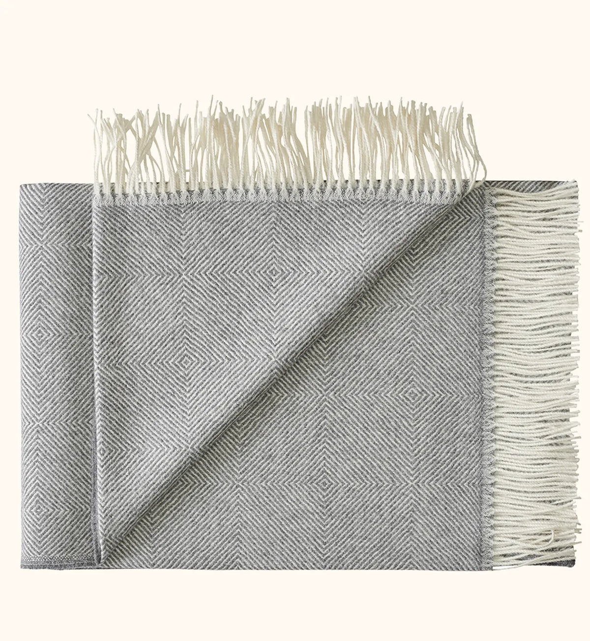 A folded gray and white woven throw blanket with a subtle geometric diamond pattern and cream-colored fringe tassels on both ends, displayed against a solid off-white background.