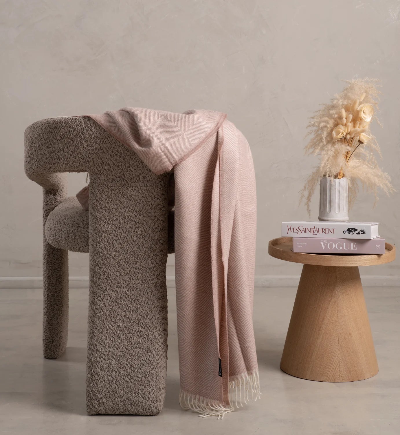 Alpaca dusty Pink blanket draped over a textured chair with a wooden side table featuring books and decor.