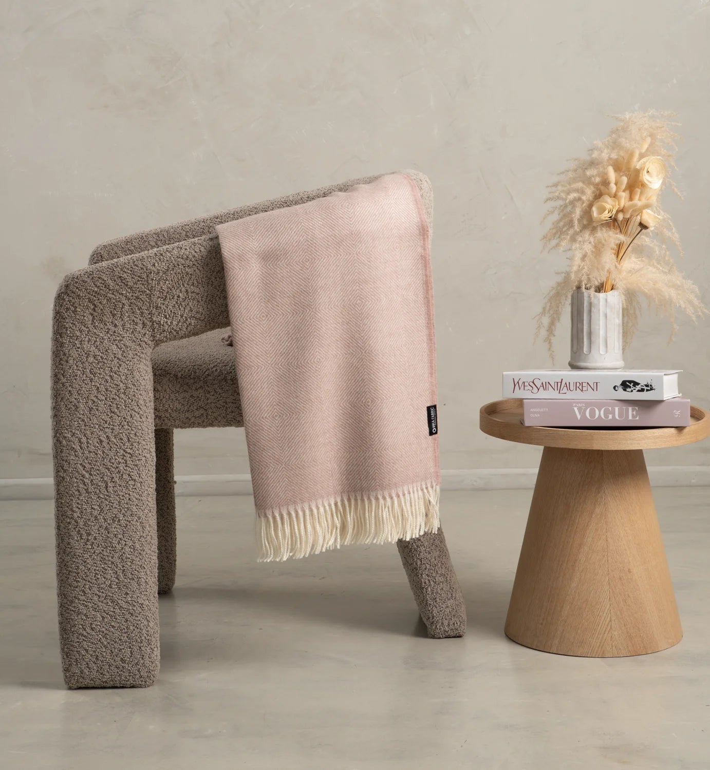 Chair with a Alpaca pink blanket draped over it next to a wooden side table with books and a plant.
