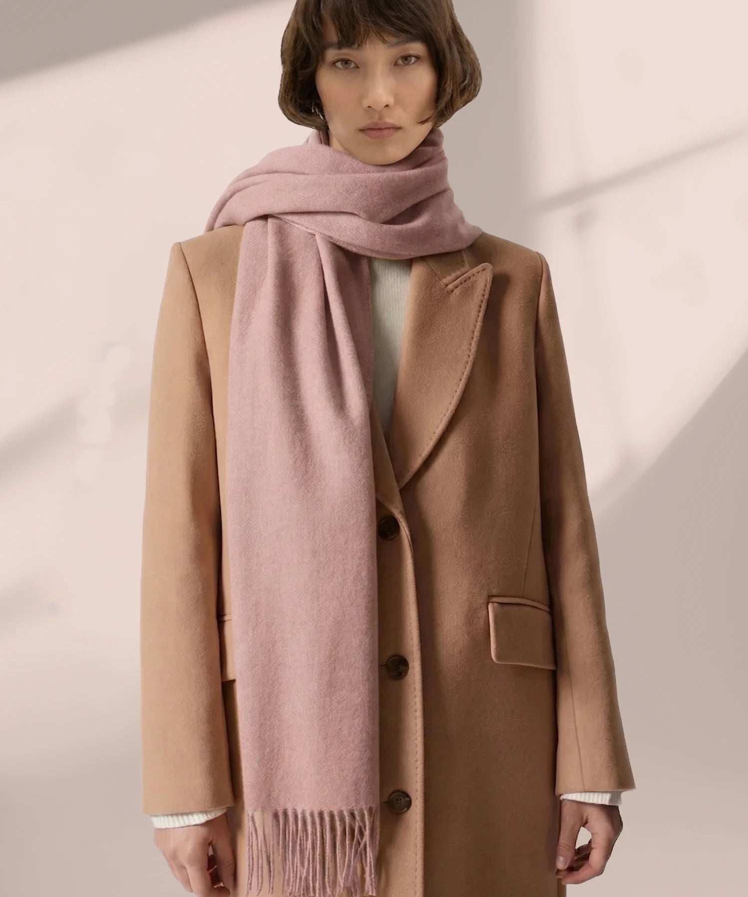 Person wearing a brown coat and pink scarf against a light background