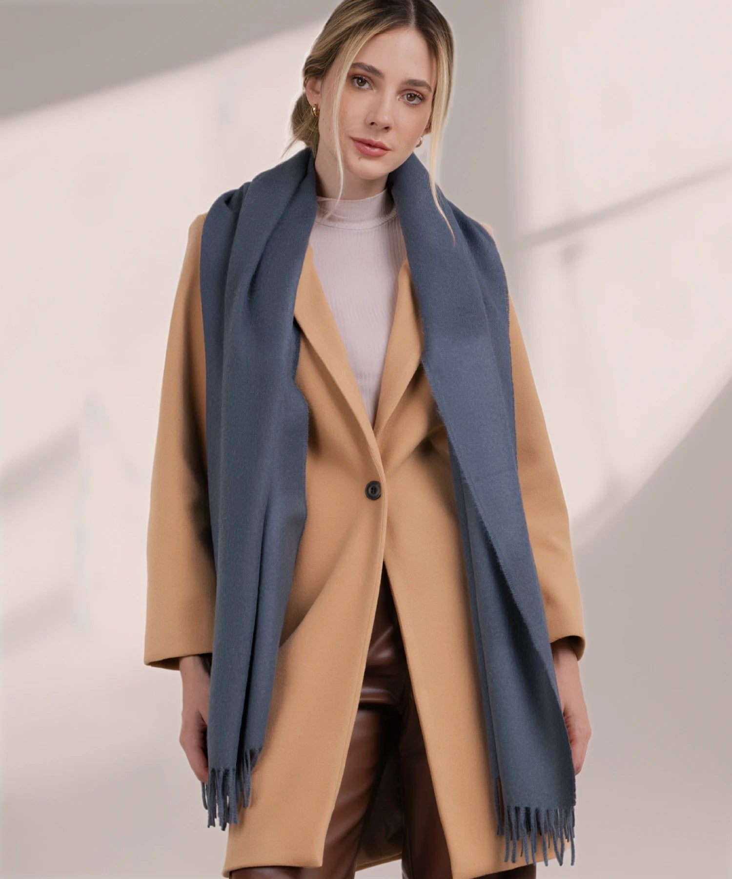 Woman wearing a beige coat with a blue scarf against a light background