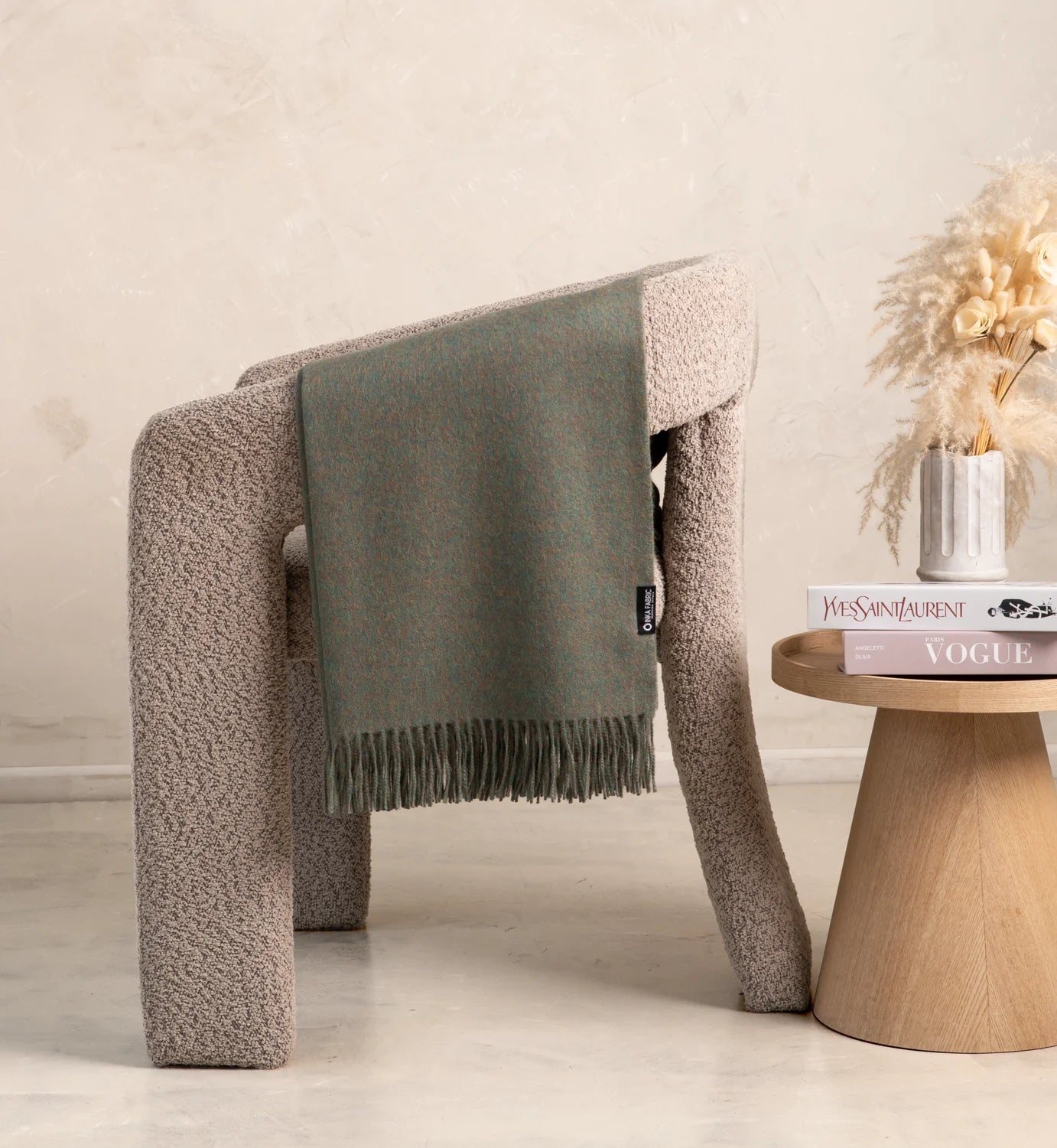 green alpaca Gray blanket draped over a textured chair next to a wooden side table with decorative items.