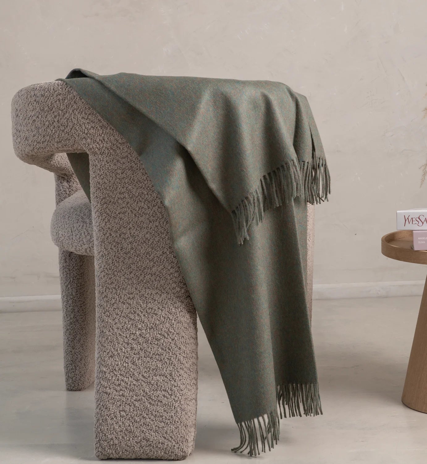 Green blanket draped over a textured chair against a neutral background