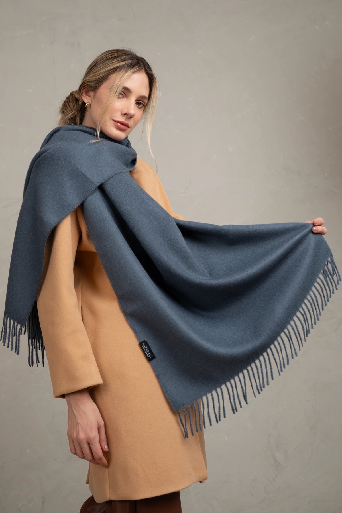 Woman wearing a alpaca blue scarf with fringe on a gray background