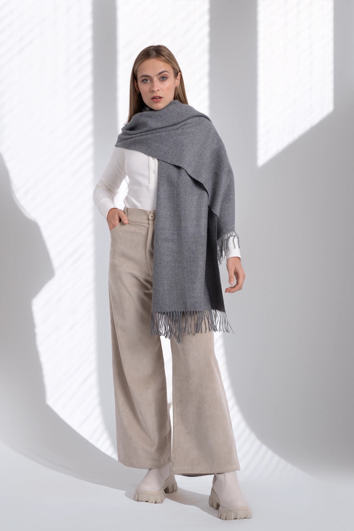 Woman wearing a gray scarf and beige pants against a white background