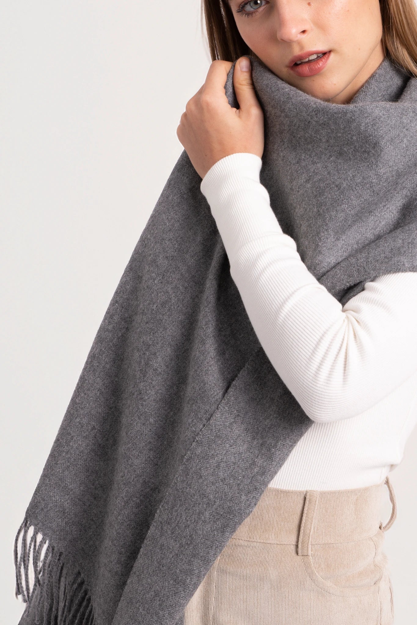 Woman wearing a gray scarf with a white shirt and beige pants on a light gray background