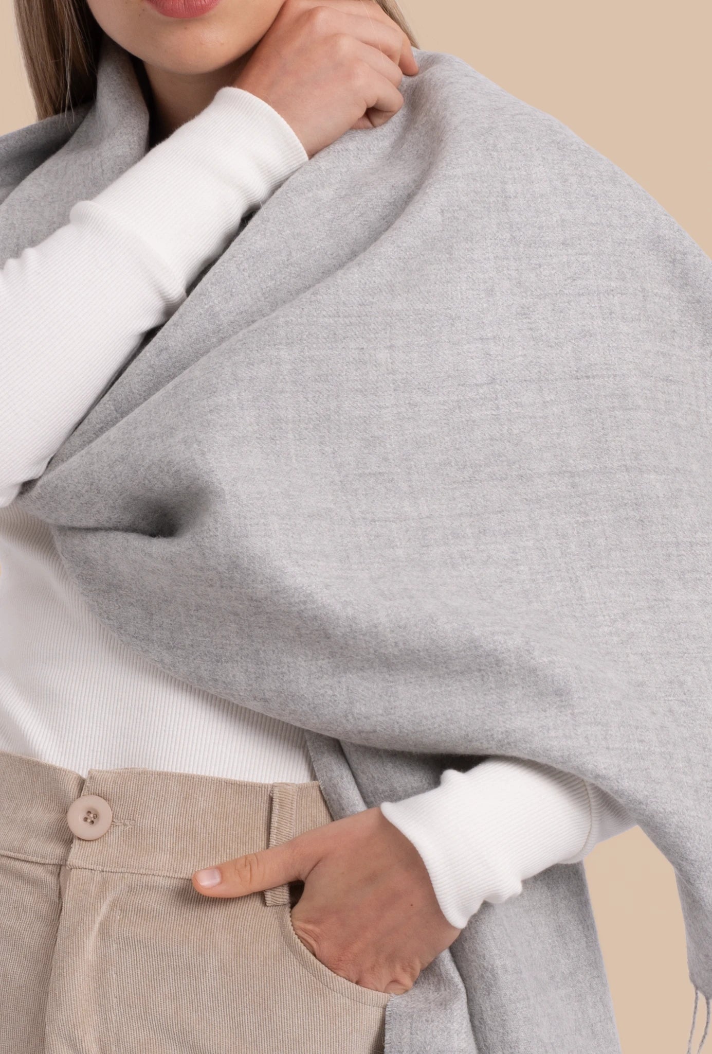 Person wearing a gray scarf over a white shirt with beige pants.