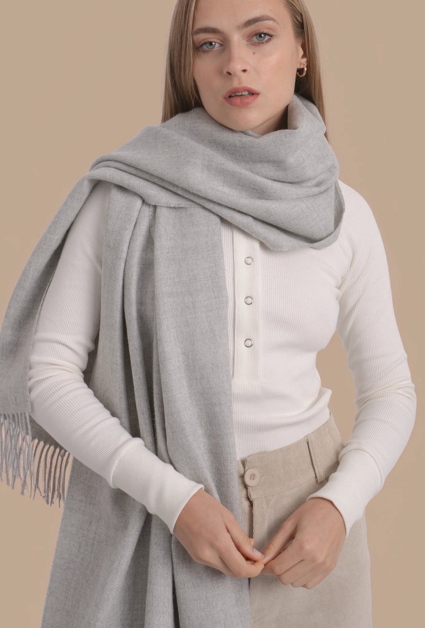 Woman wearing a gray scarf and white sweater against a beige background