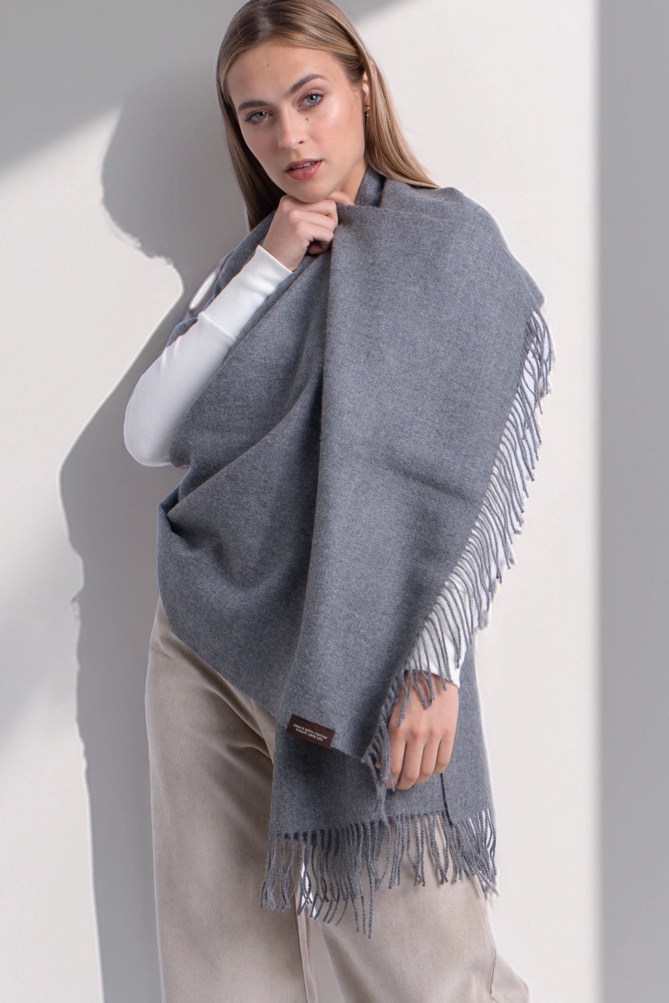 Woman wearing a gray shawl with fringes on a white background