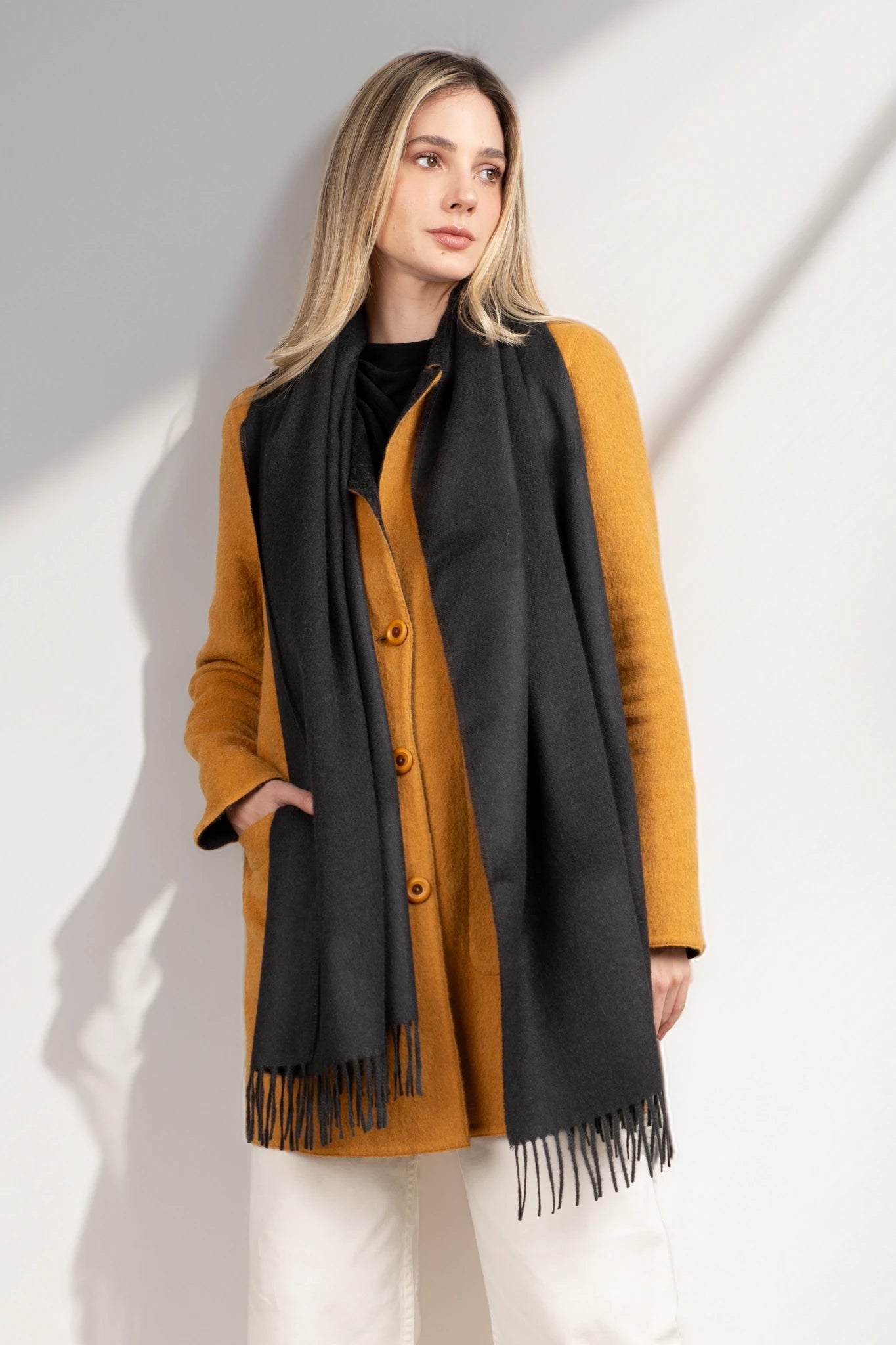 Woman wearing a mustard yellow coat and black scarf on a white background