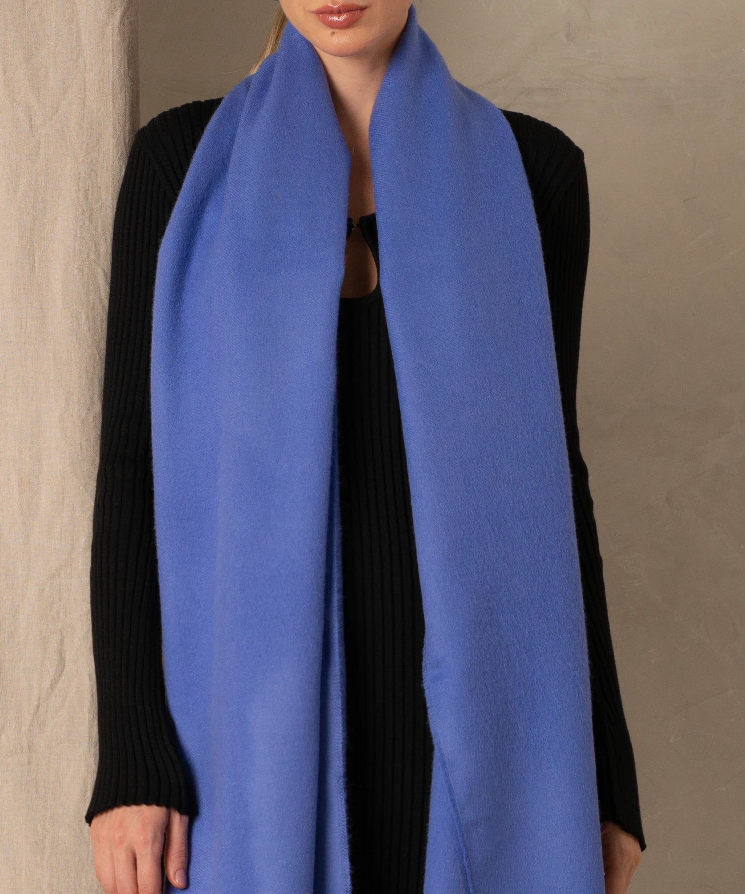Person wearing a long blue scarf with a plain background