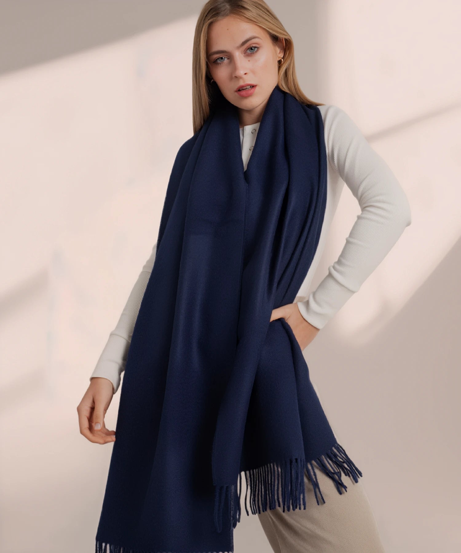 Woman wearing a navy blue scarf with fringe on a beige background