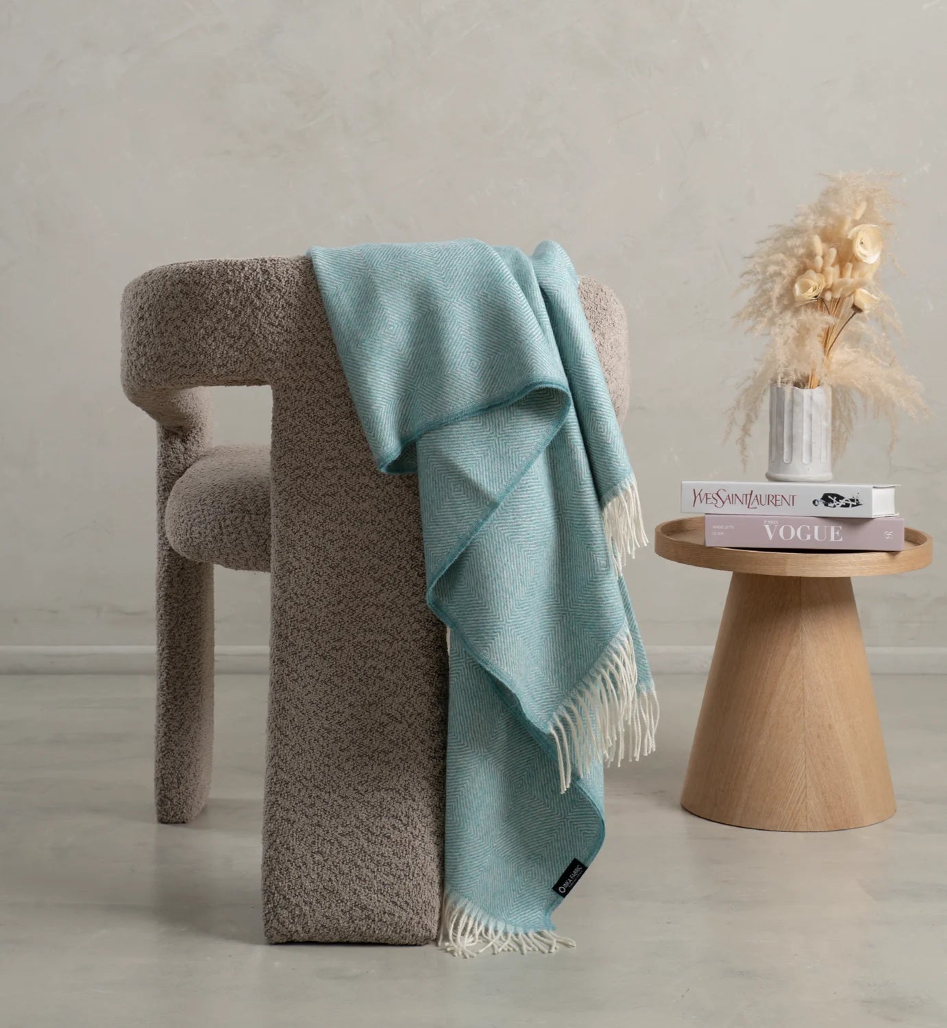 Light blue alpaca throw blanket draped over a textured brown chair with a wooden side table in the background.