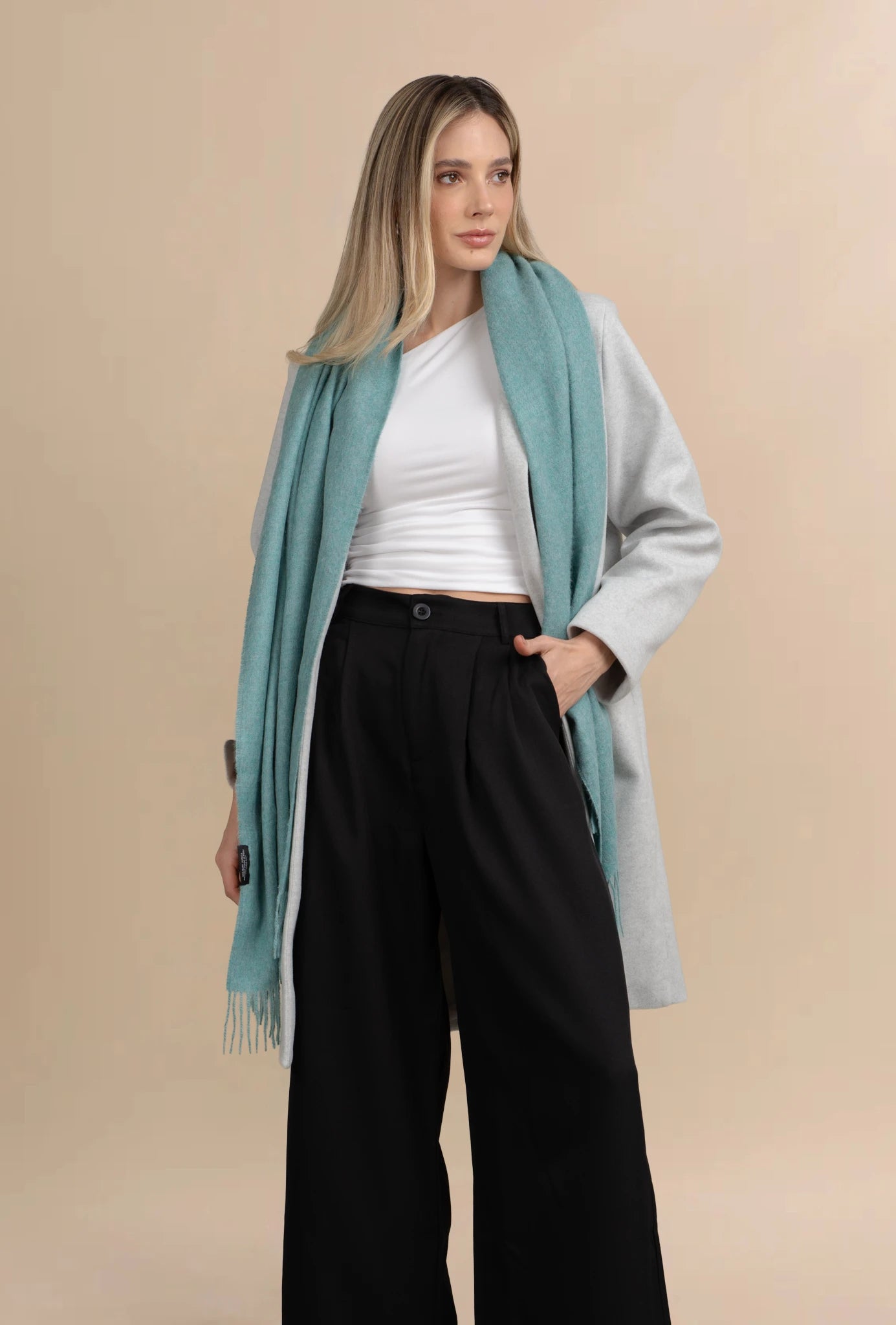 Woman wearing a light blue scarf, white top, and black pants on a beige background