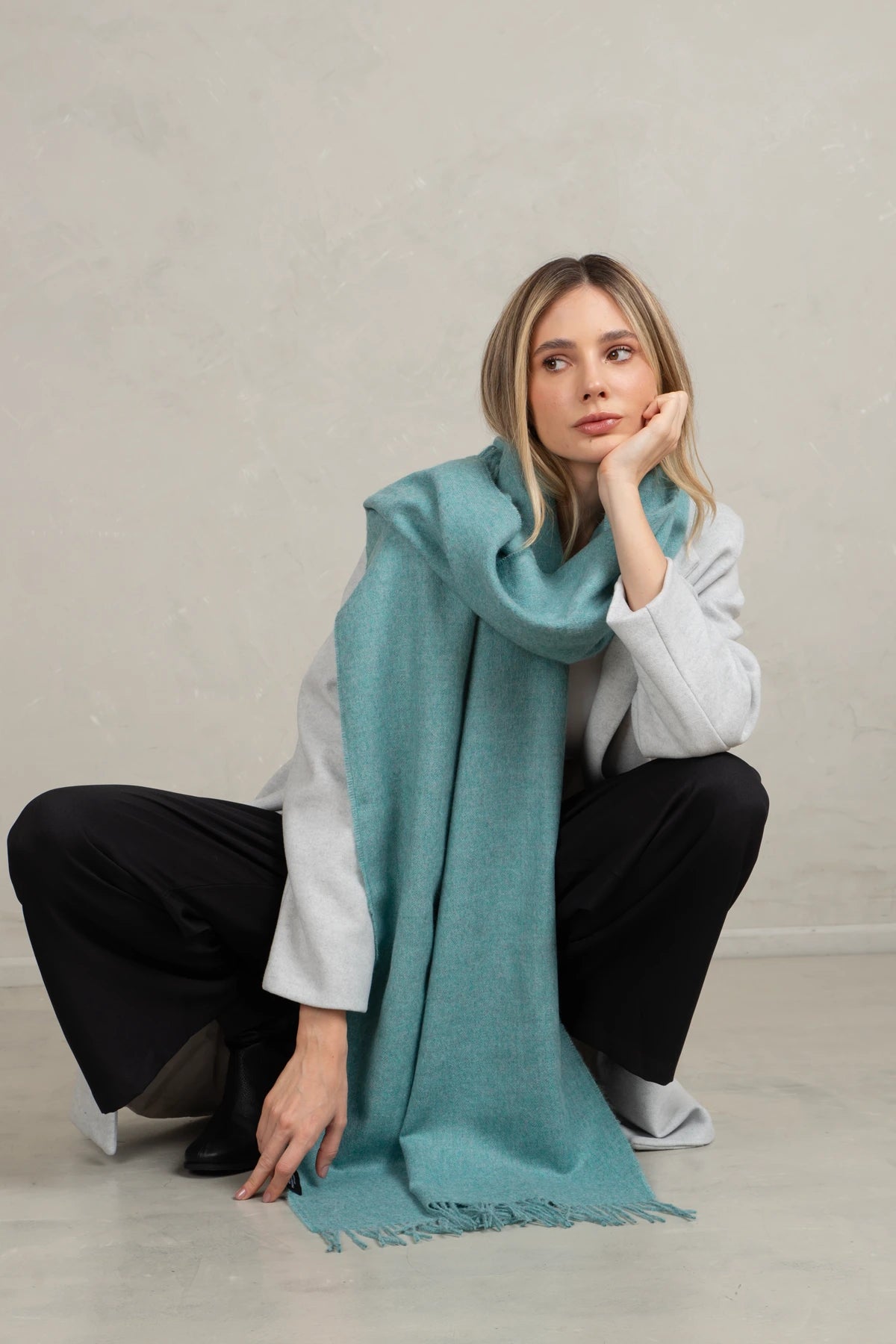 Woman wearing a light blue scarf sitting on the floor against a plain background