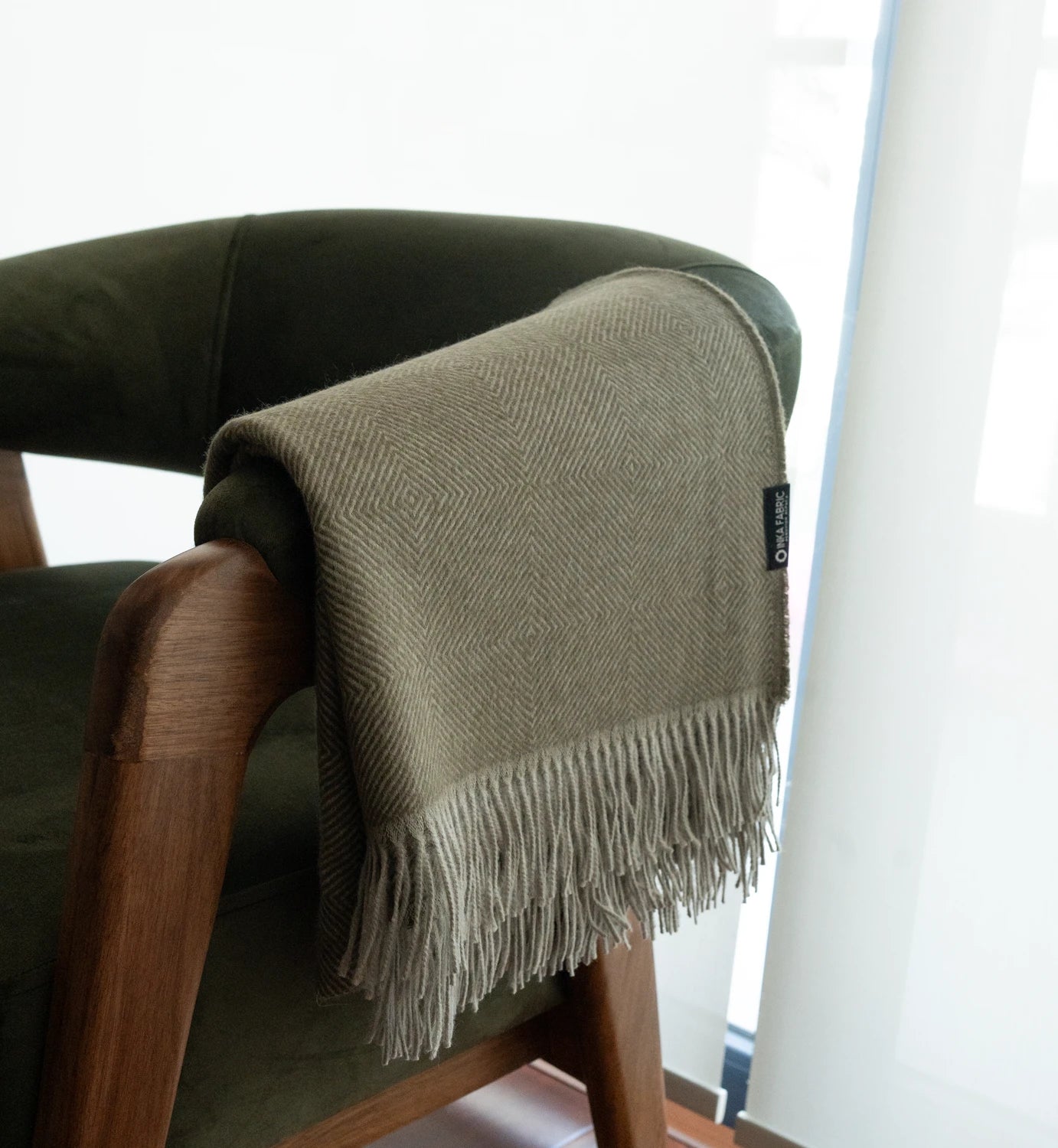 Green blanket with fringes draped over a chair next to a window
