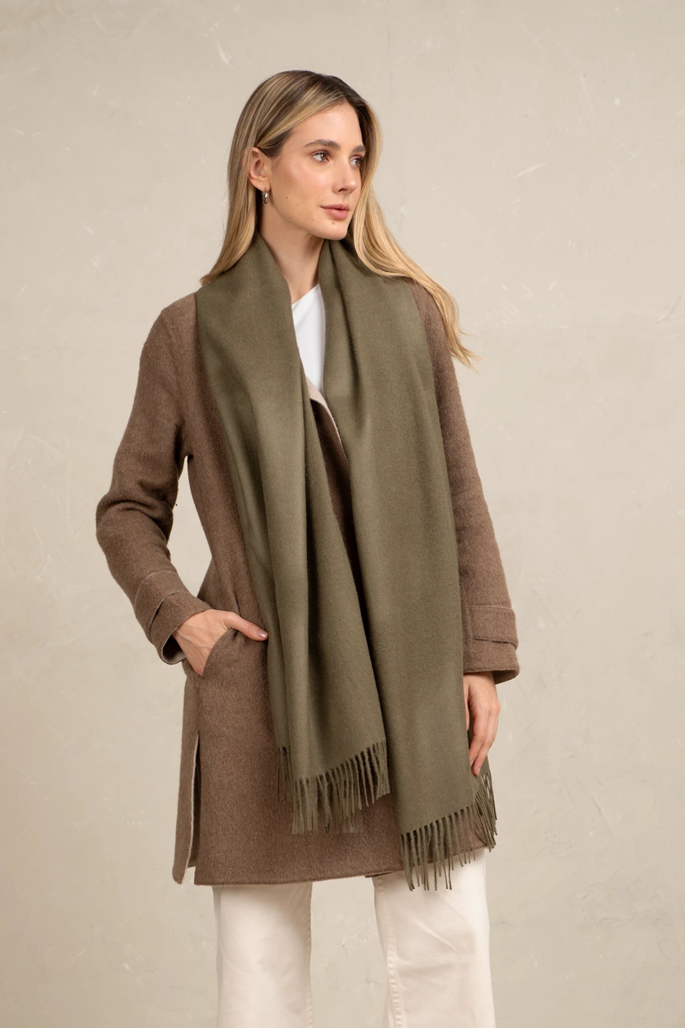 Woman wearing a brown coat and green scarf against a beige background