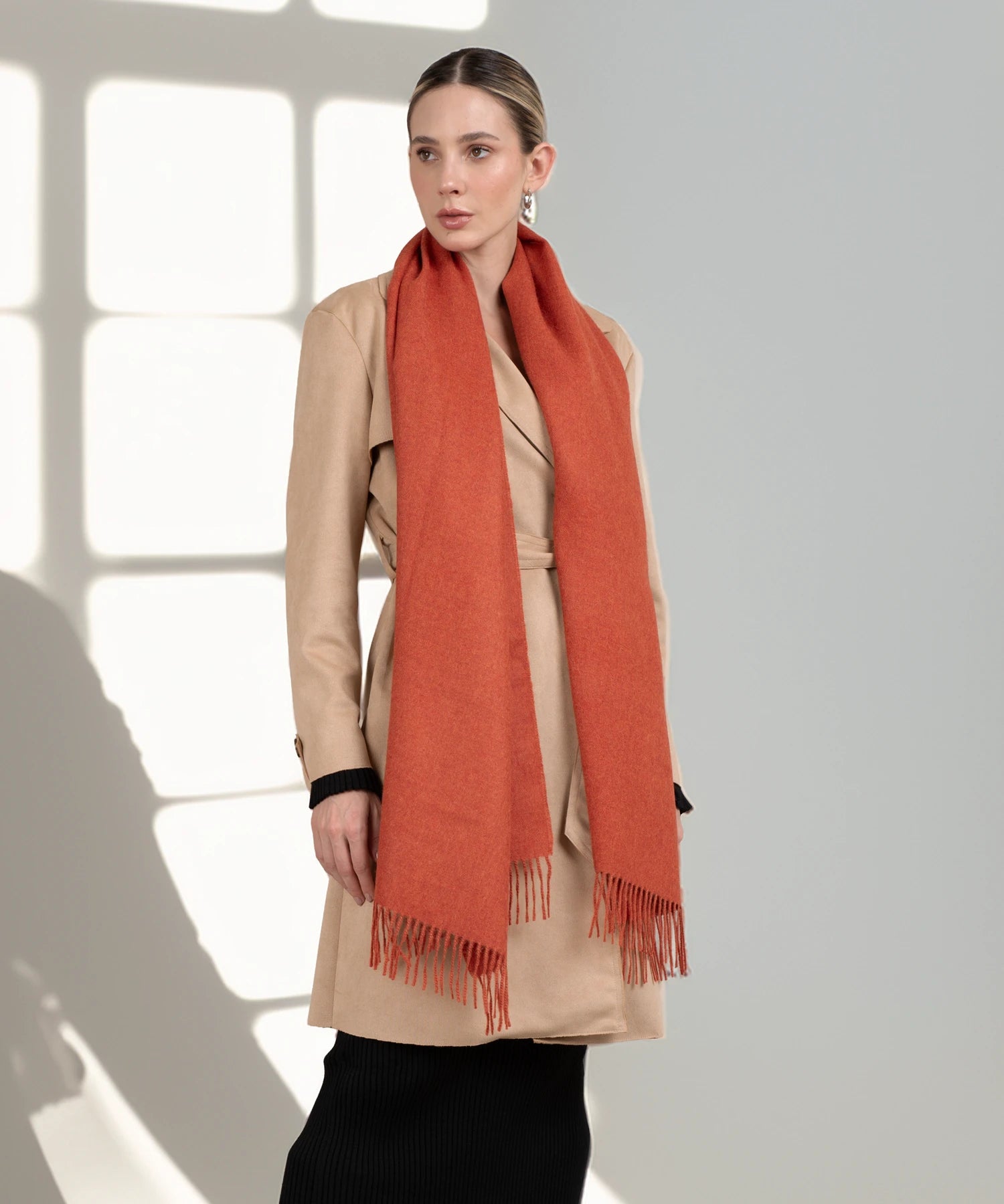 Woman wearing a beige coat and orange scarf in a bright room