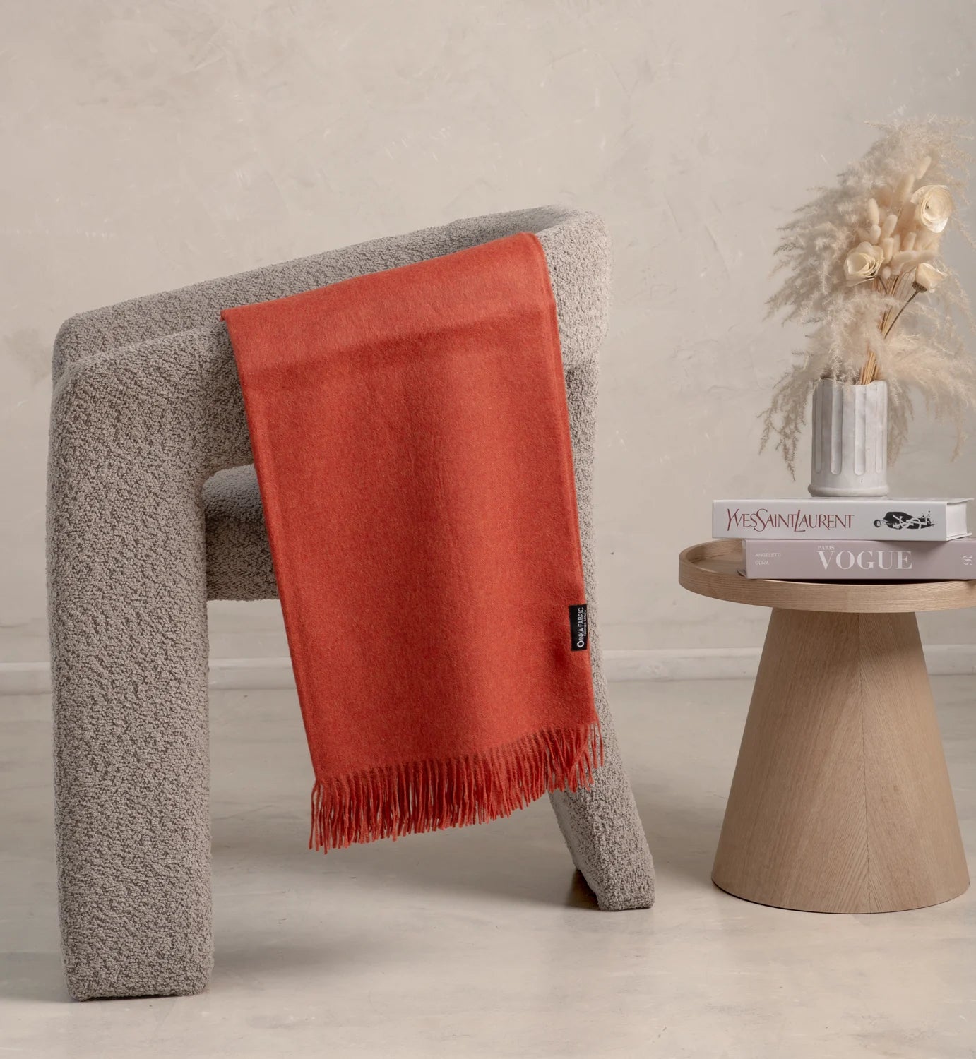 Alpaca Red blanket draped over a textured gray chair with a wooden side table in the background.