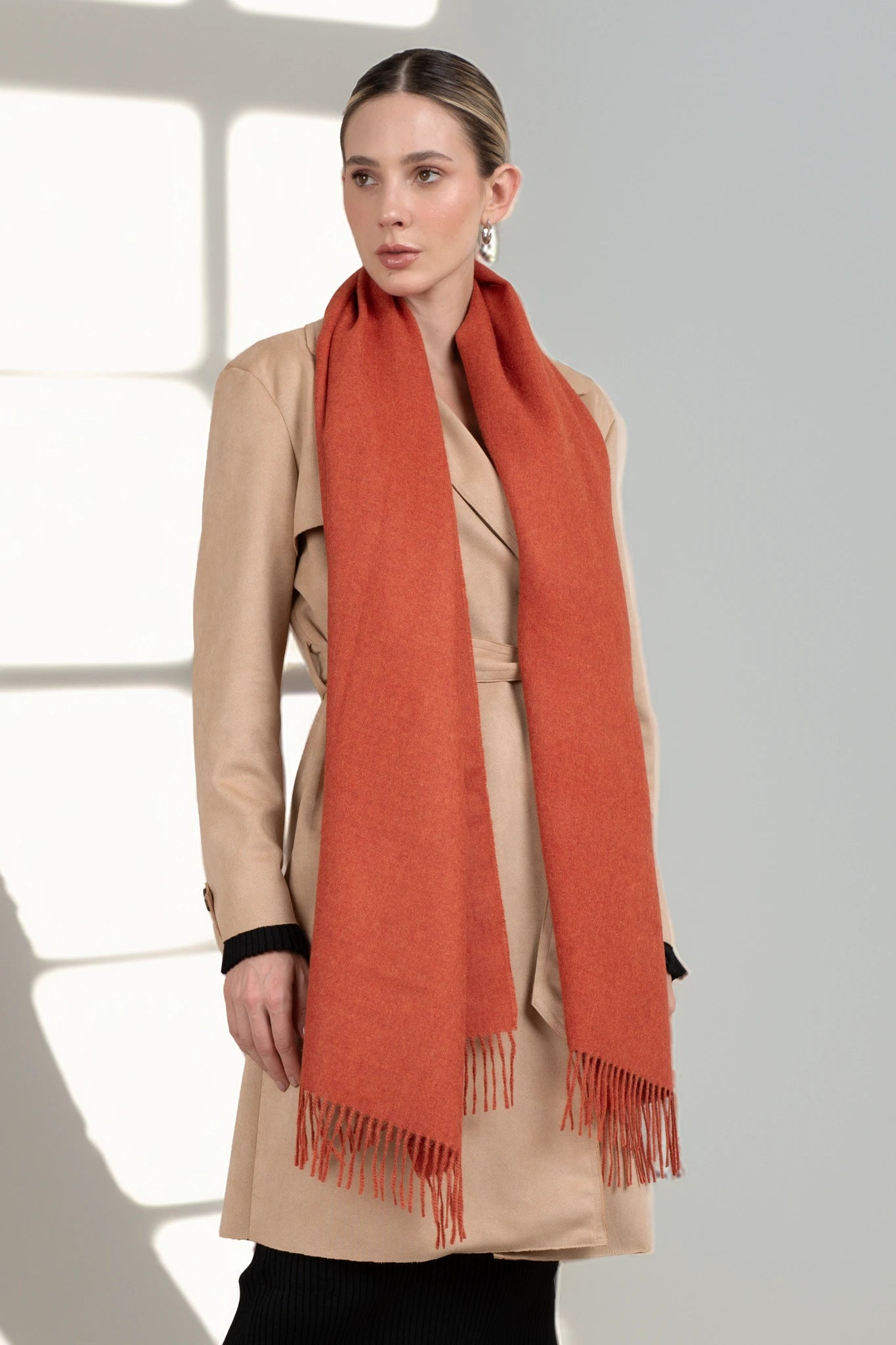 Woman wearing a beige coat and orange scarf against a light background